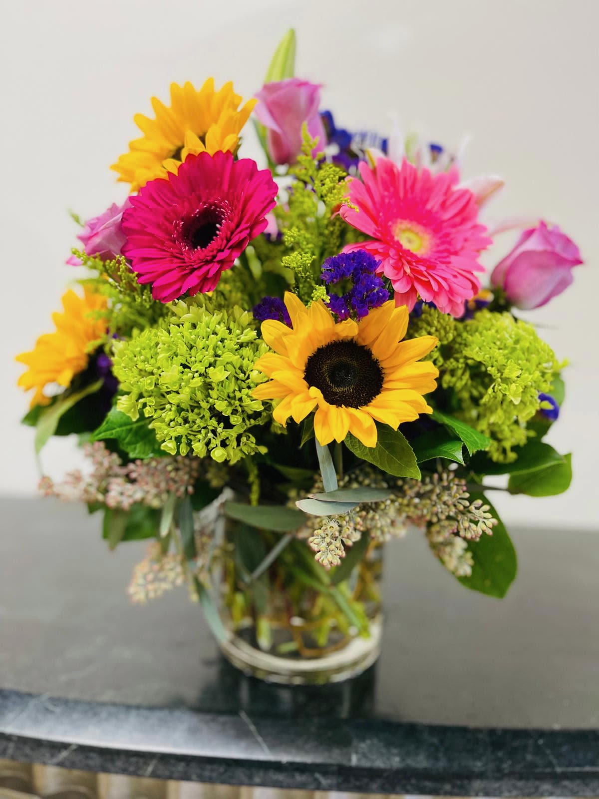 Mixed bouquet with sunflowers, pink gerberas, and roses in a glass vase