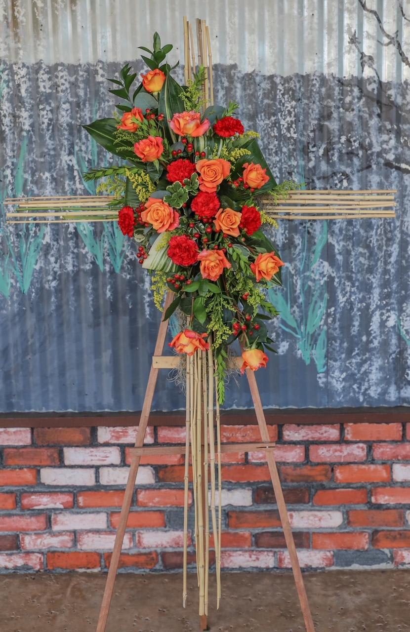 Tall floral standing arrangement with orange roses and red carnations on an easel