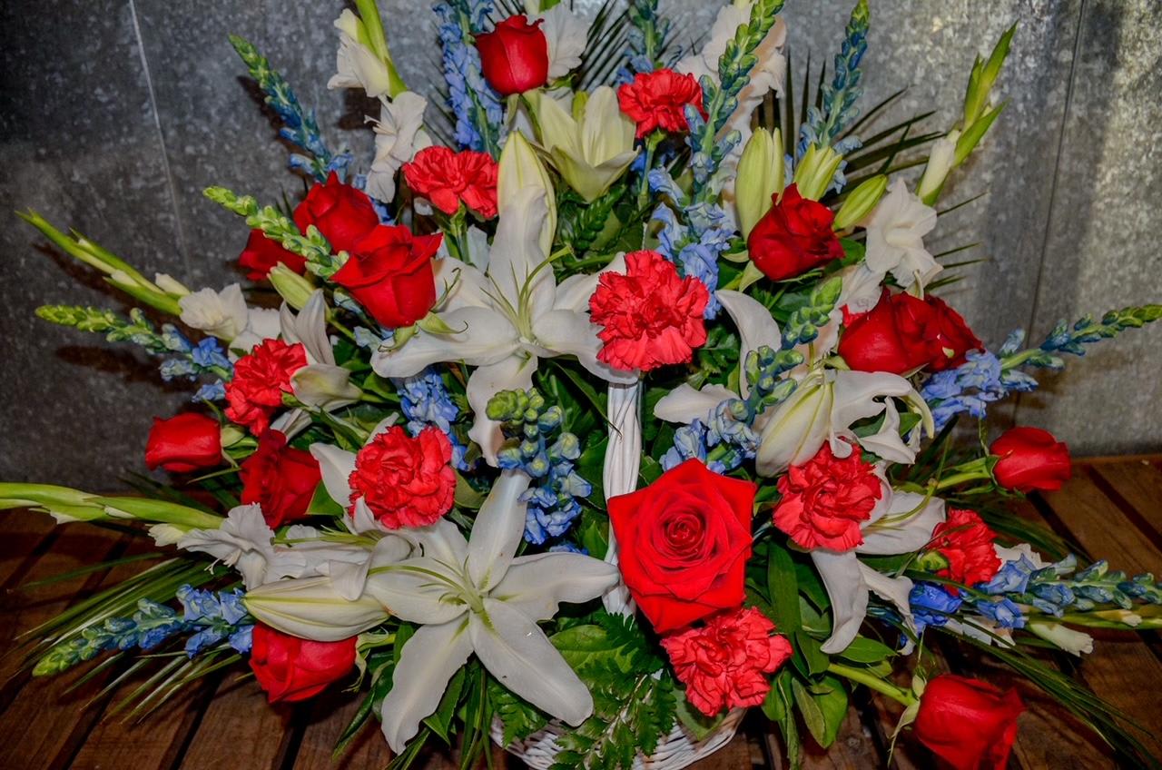 Red roses, white lilies, and blue flowers in a basket arrangement