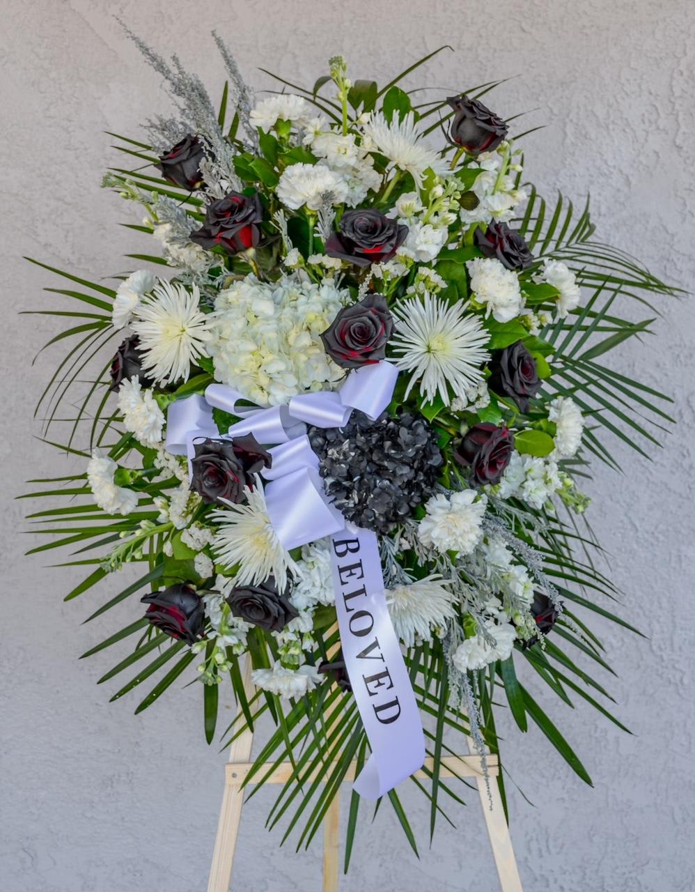 Standing funeral wreath of white flowers and dark roses with a ribbon