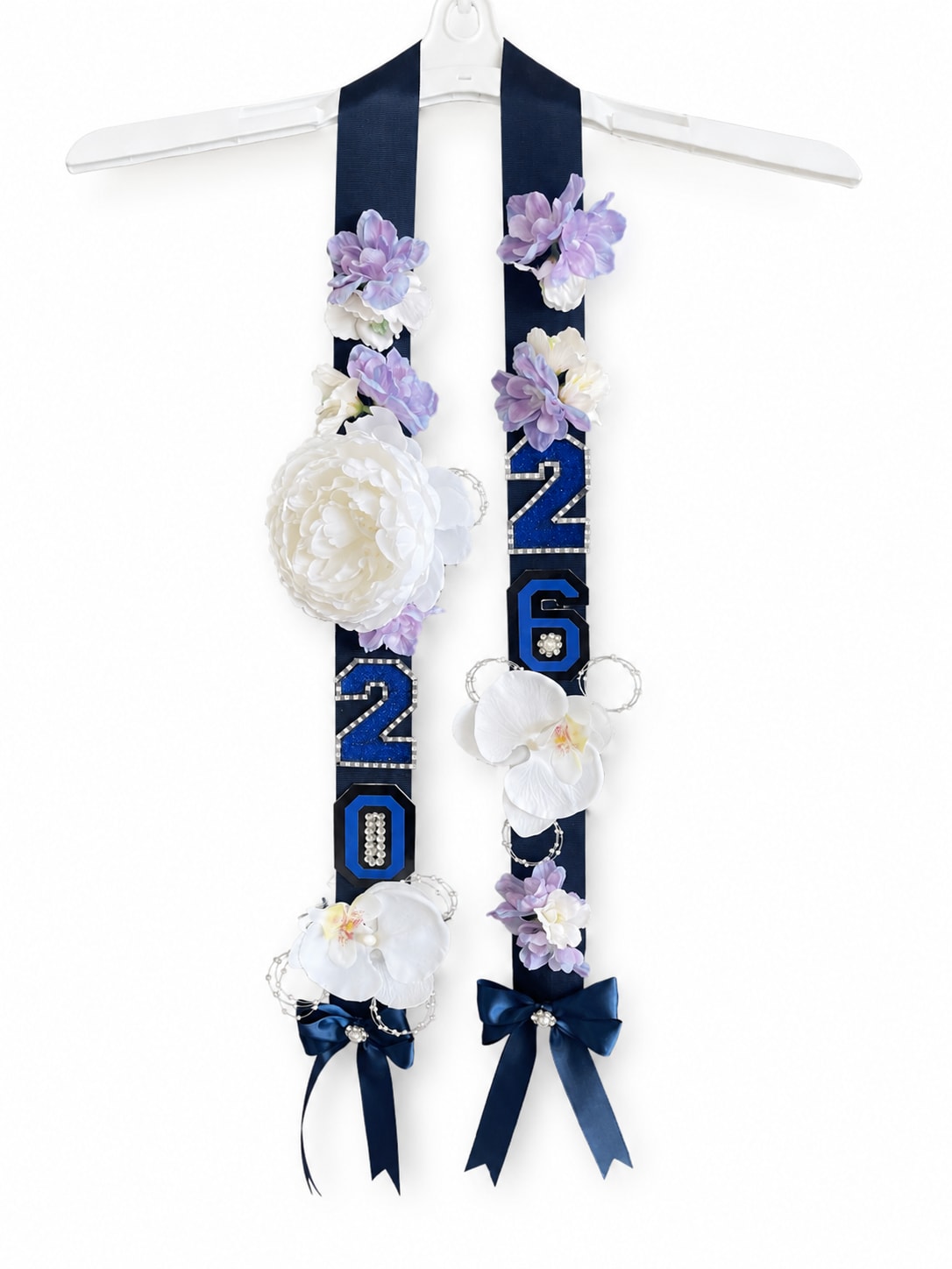 Navy Blue 2026 Ribbon Lei - Elegant handmade graduation ribbon lei featuring navy satin ribbons, sparkling “2026” accents, Silk lavender florals, white orchid details, and satin bows. A beautiful keepsake designed to celebrate your graduate in style. Perfect for senior photos, graduation ceremonies, and gift giving. Lightweight, stylish, and can last a lifetime, handcrafted with attention to every detail. 30in long