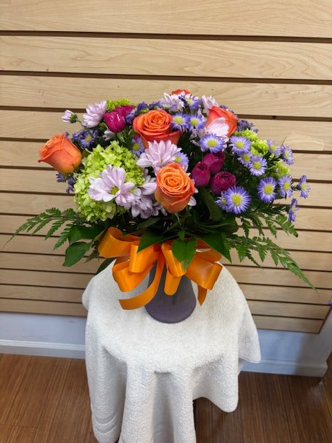 Bouquet of orange roses and purple daisies in a vase with an orange ribbon