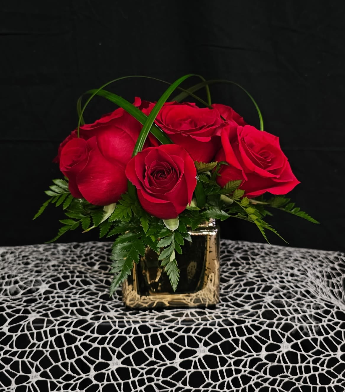 Red roses arranged in a gold square vase with green foliage