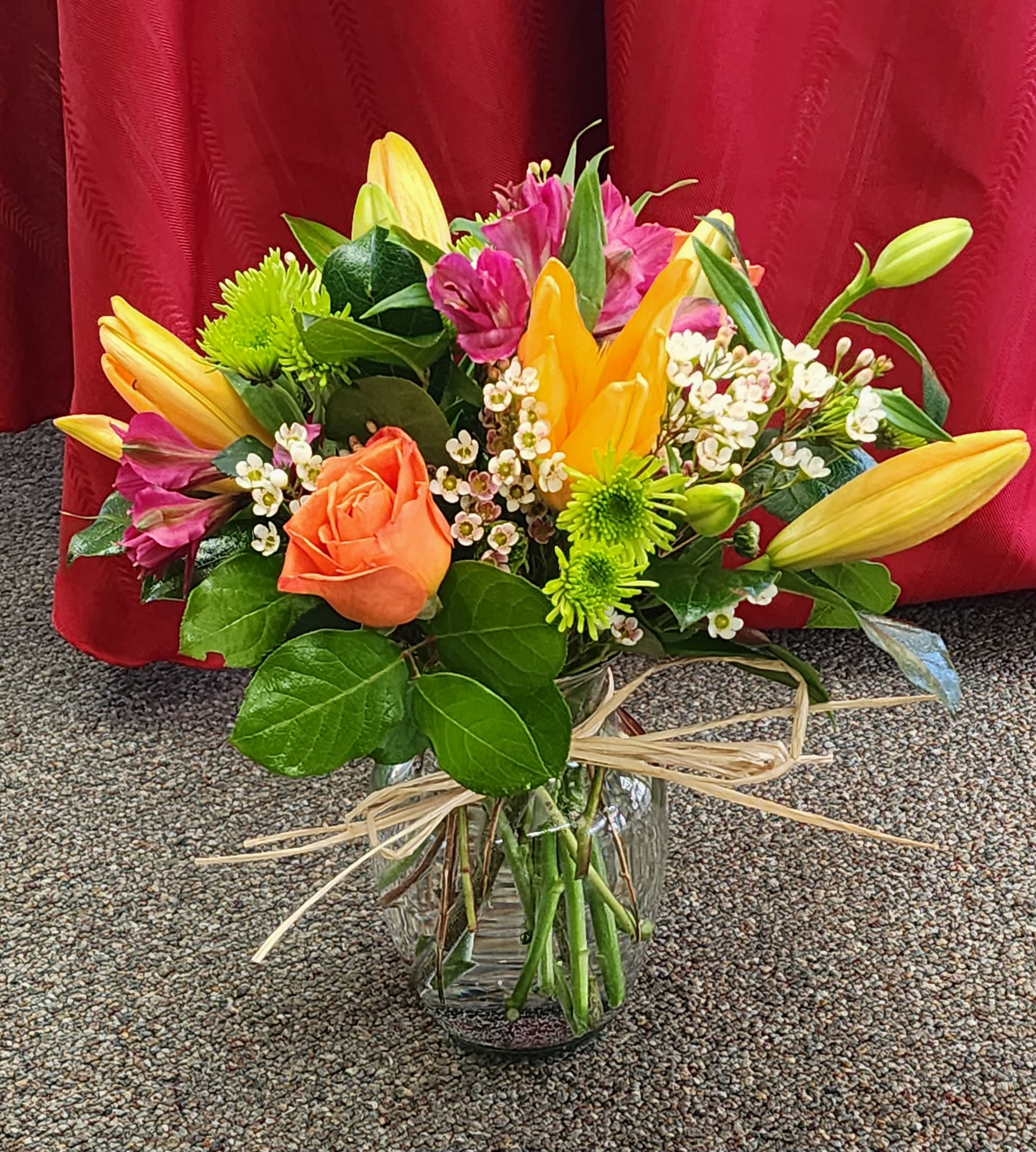 Mixed bouquet of lilies, roses, and small white flowers in a glass vase