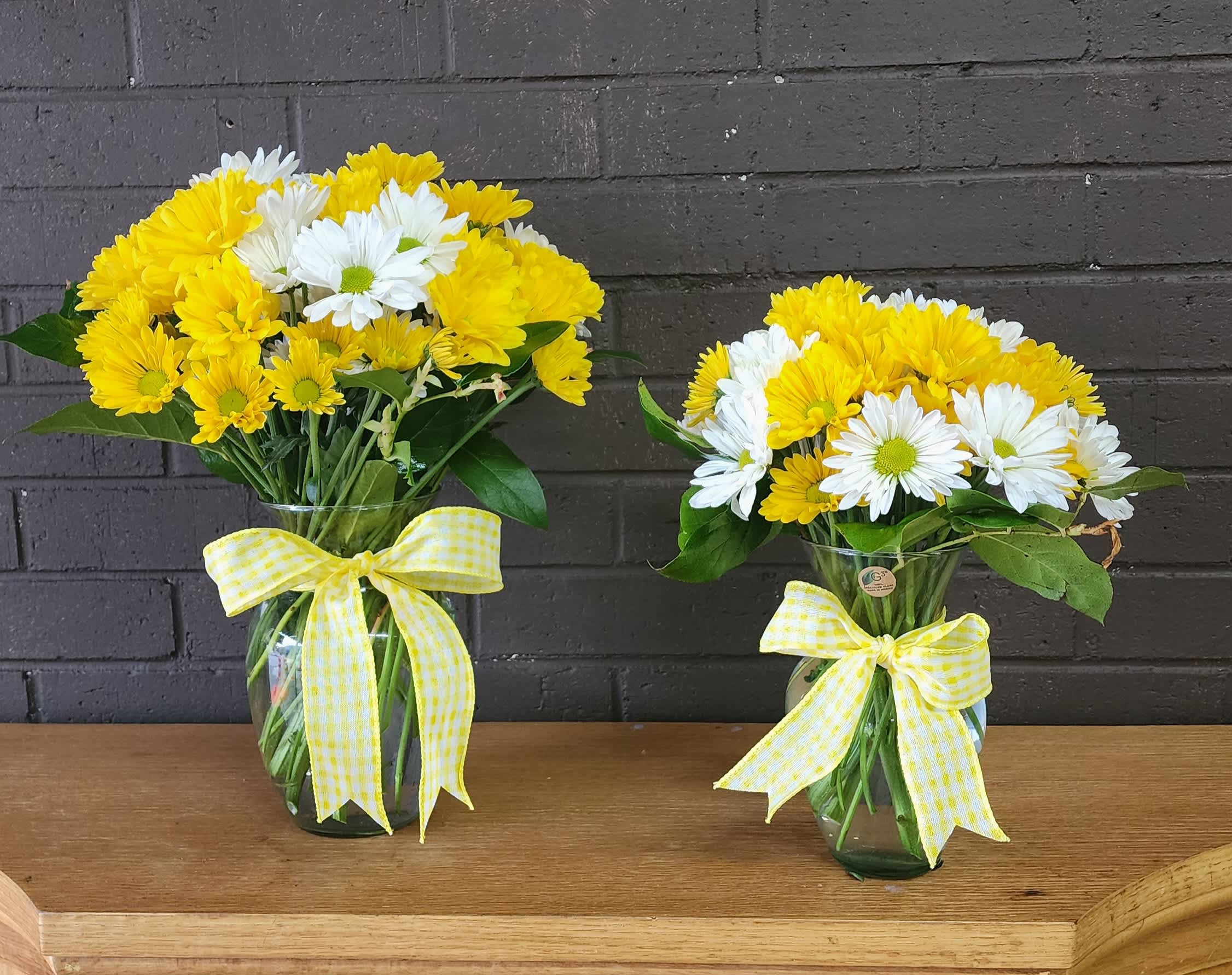 Two yellow and white daisy bouquets in glass vases with ribbon bows