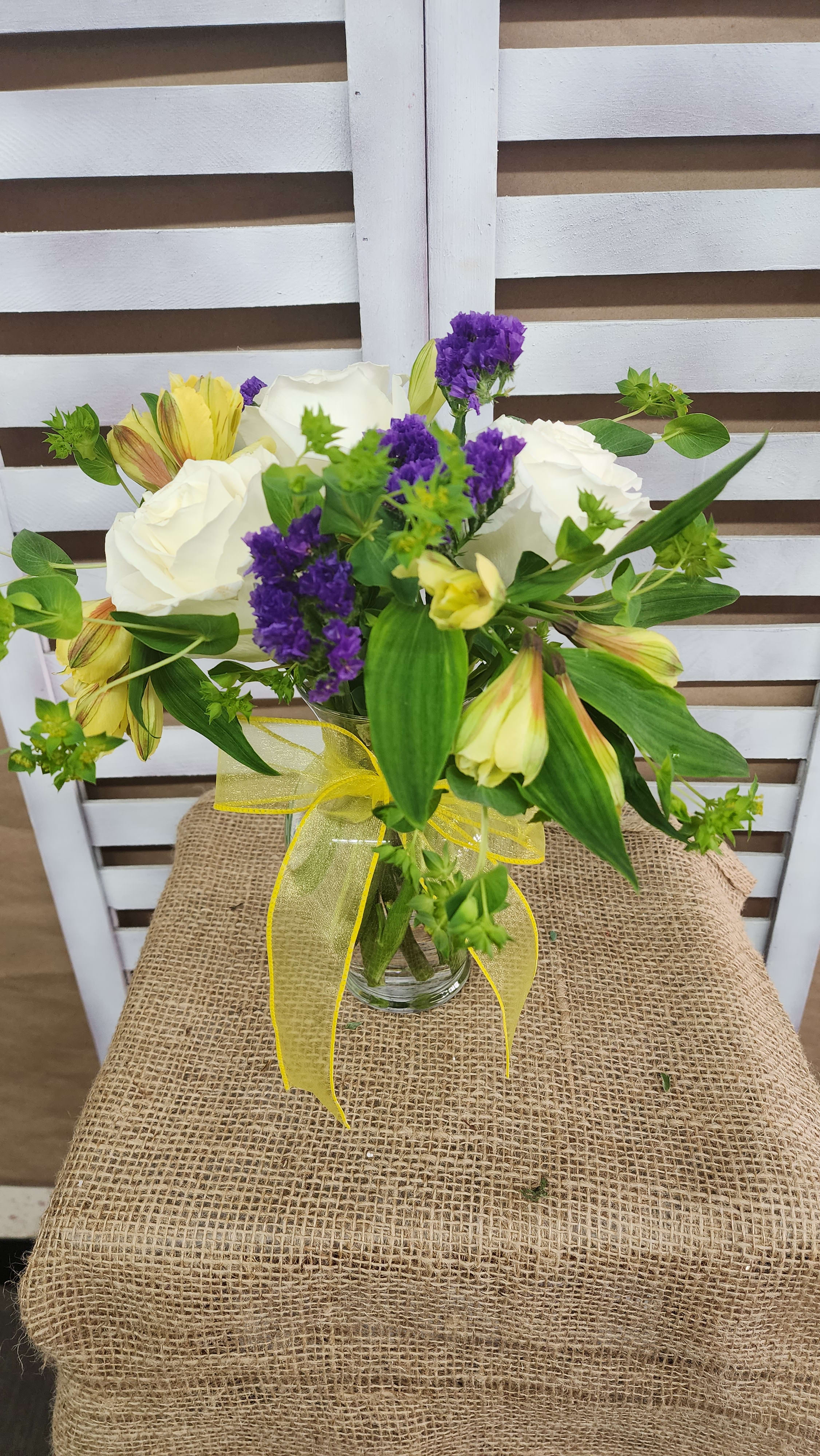 Bouquet of white roses, purple filler flowers, and yellow alstroemeria in a glass vase