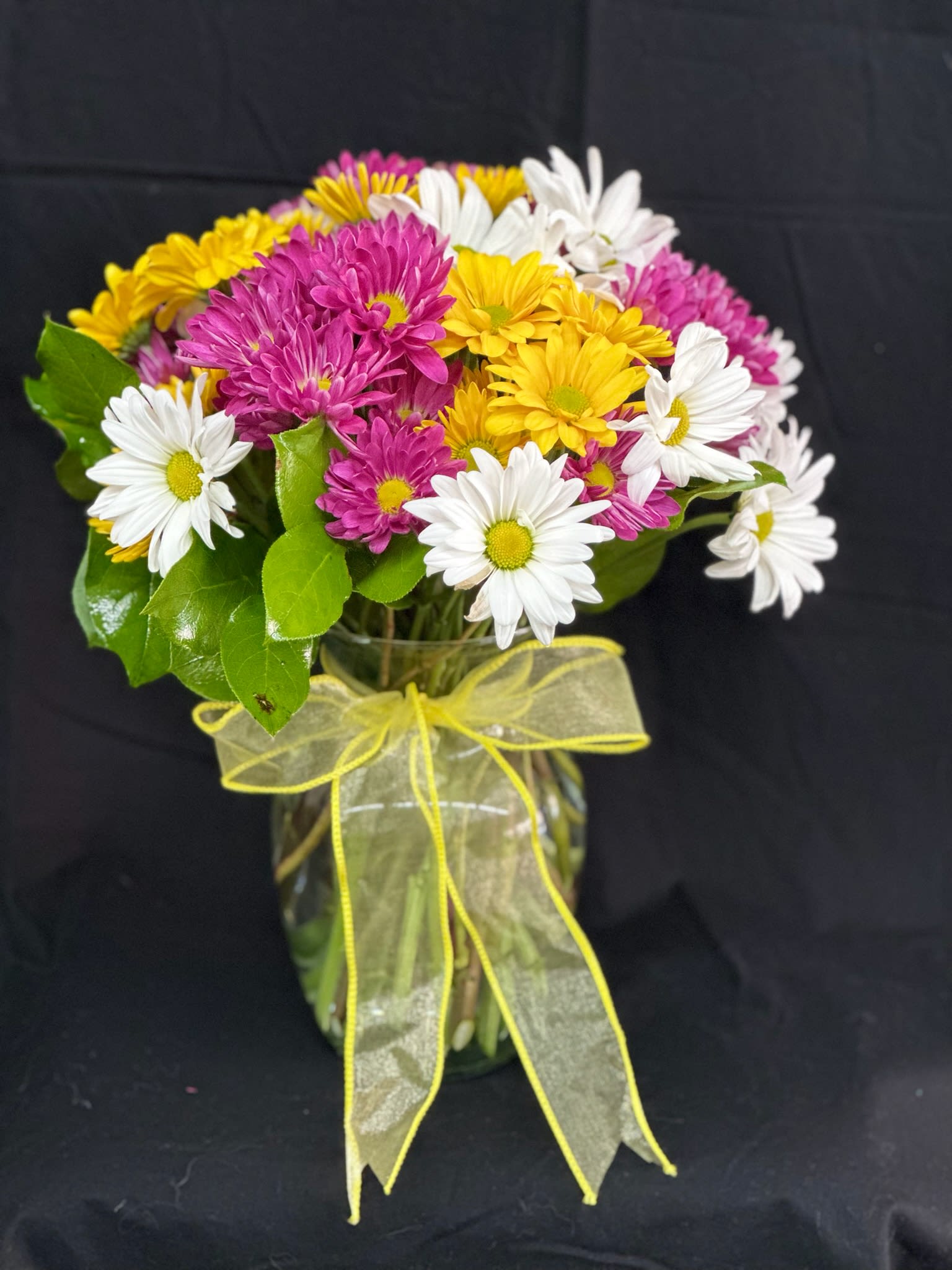 Bouquet of white, yellow, and pink daisies in a glass vase with a yellow ribbon