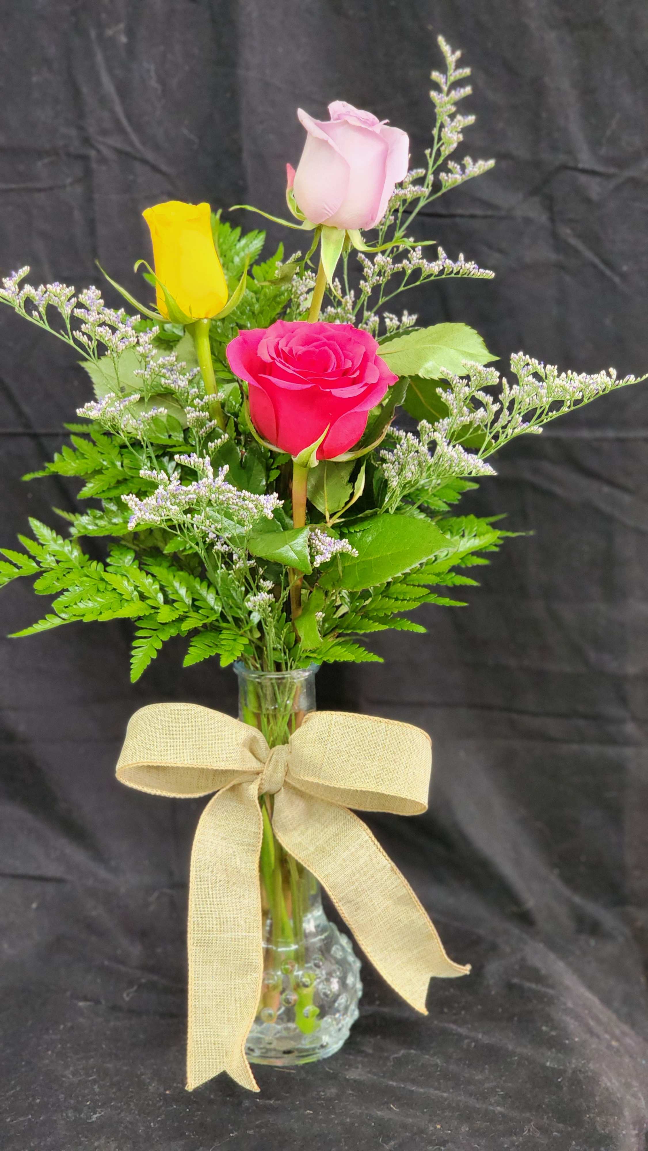 Three roses in a clear glass vase with a beige bow