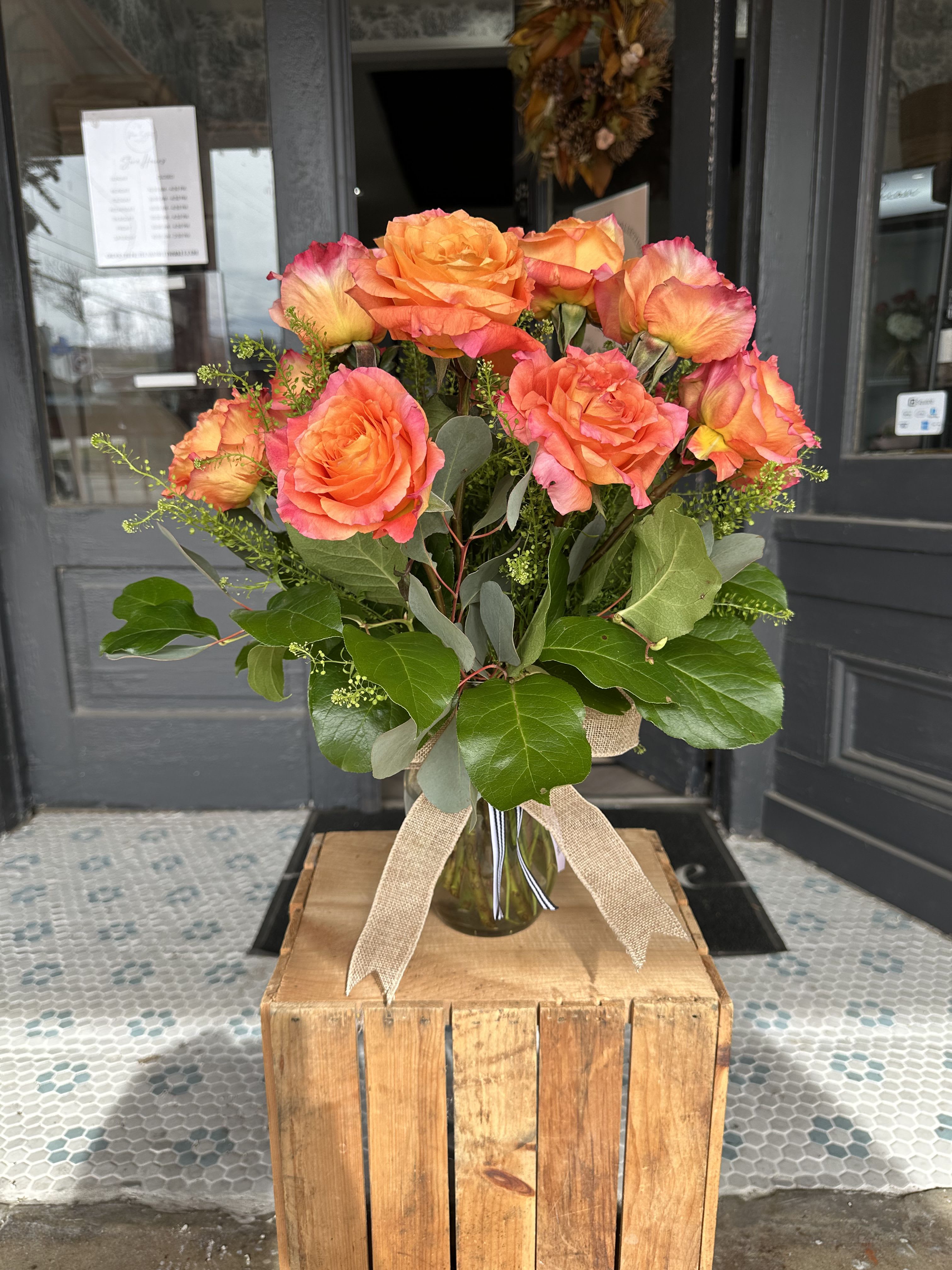 Bouquet of orange roses in a glass vase with a burlap ribbon
