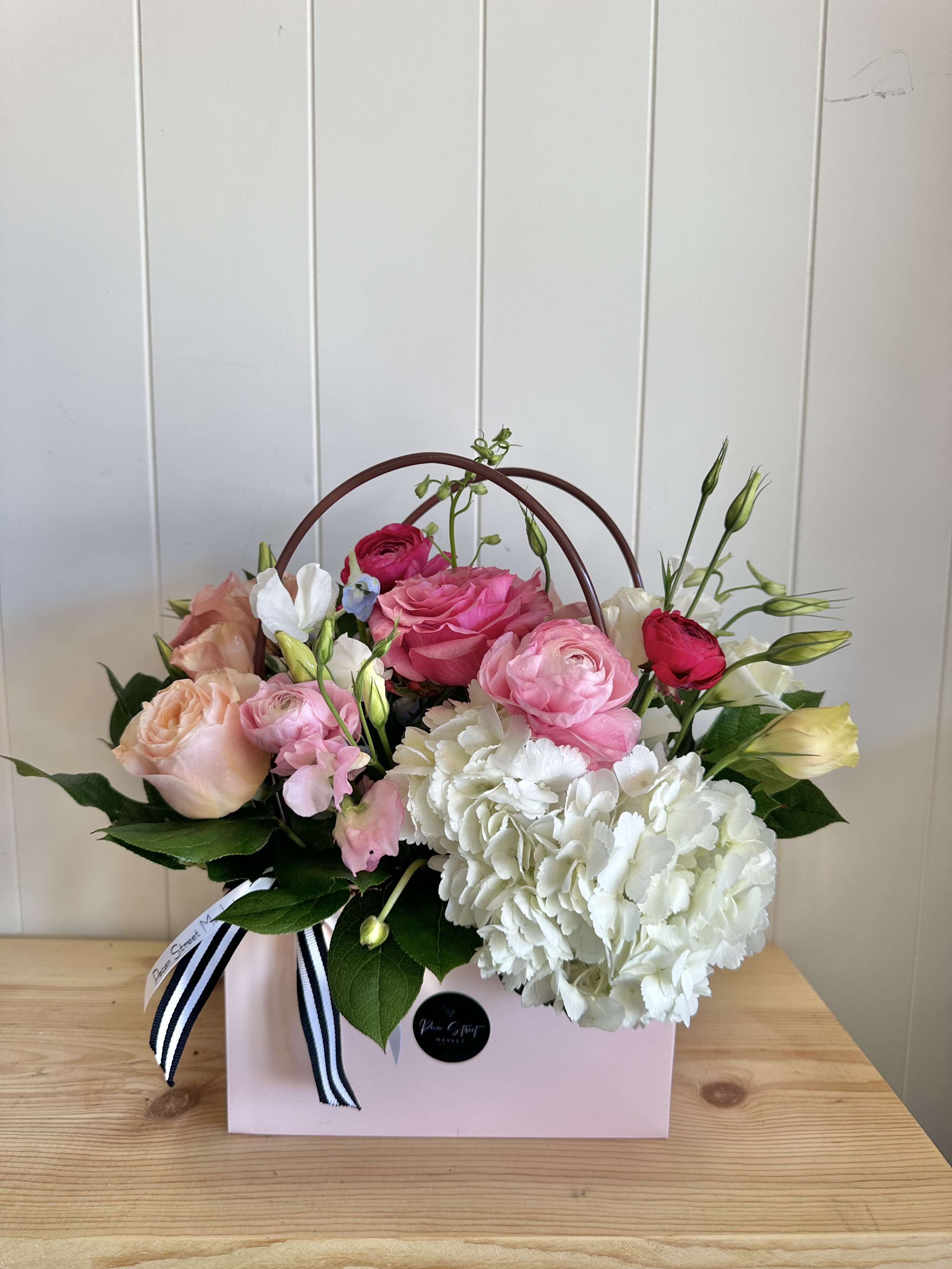 Pink and white floral arrangement in a pink gift box with ribbon handles