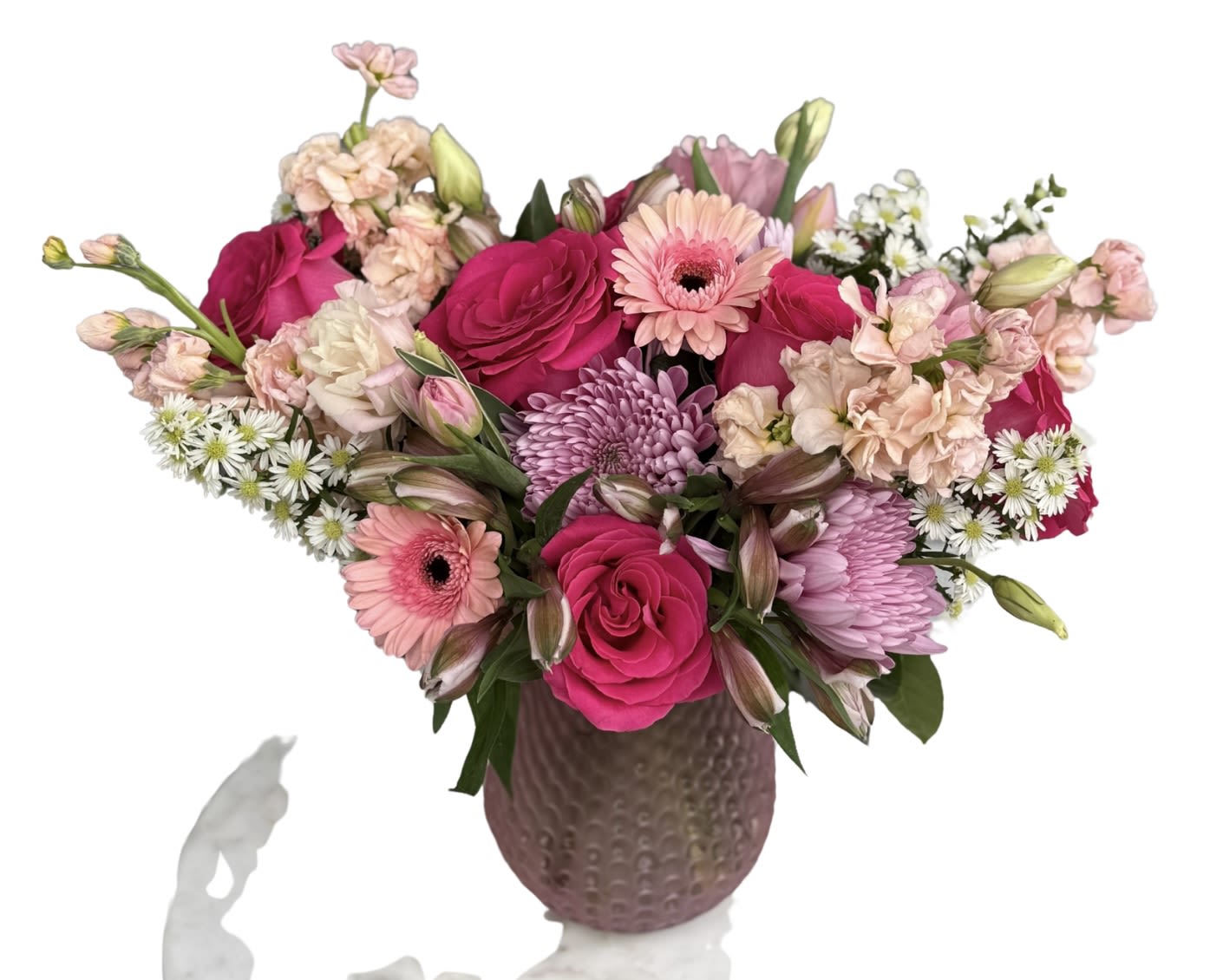 bushing blooms by local florist - A lush, rounded arrangement that feels like a warm hug - perfect as a Mother's Day flower arrangement or a cheerful everyday gift for the mom in your life. The mix of bright pink roses and pale pink gerbera daisies creates an immediate sense of celebration, while lavender chrysanthemums and soft peach stock add soft contrast and romantic depth so she'll feel truly seen.  This bouquet combines alstroemeria, lisianthus, roses, gerbera, chrysanthemums, stock and delicate white filler blooms in a feminine pink-peach-white-purple palette. The dense layering gives the arrangement an abundant, garden-fresh texture, and it's presented in a textured mauve ceramic vase that doubles as a keepsake decorative piece.  Ideal for moms who appreciate both classic romance and modern style, this arrangement works for Mother's Day, birthdays, or "just because" moments. Vase dimensions and exact flower counts are provided at checkout; to keep blooms fresh, change the water every 2-3 days and trim stems slightly when you do.