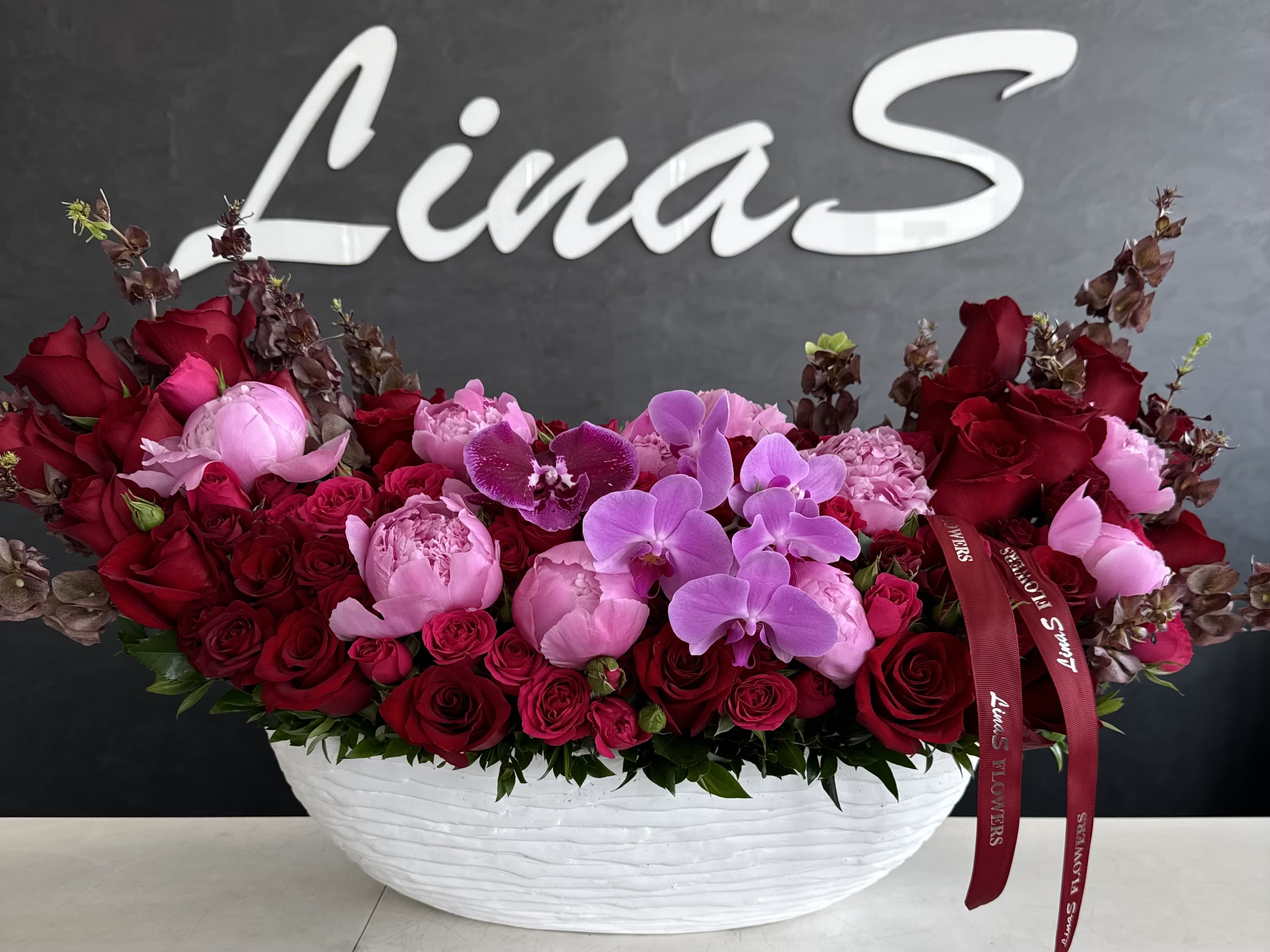 Crimson Blush Elegance - A luxurious arrangement of soft pink peonies, elegant pink Phalaenopsis orchids, and passionate red roses — a perfect harmony of romance, beauty, and timeless elegance.