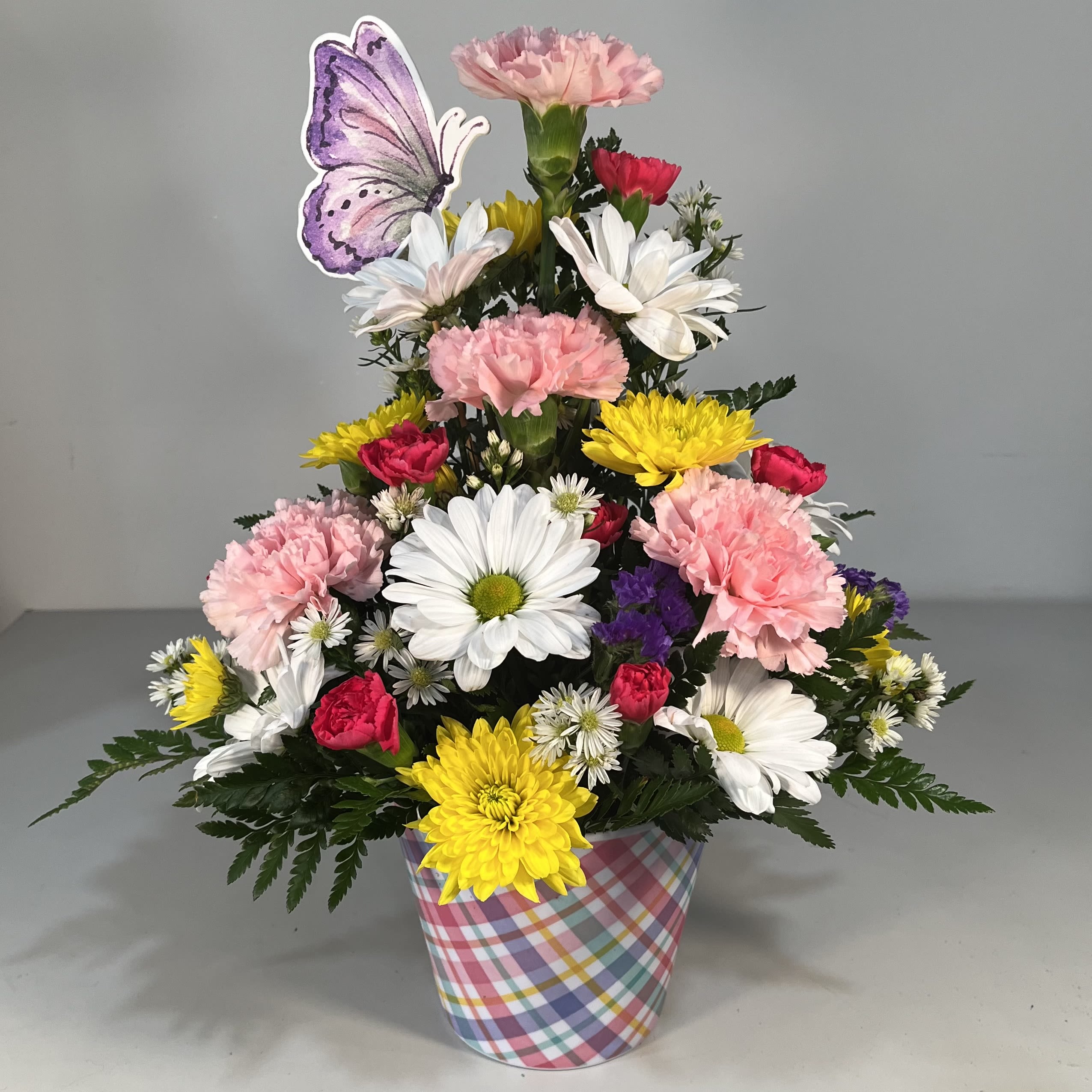 Colorful mixed flower arrangement in a plaid container with a butterfly pick