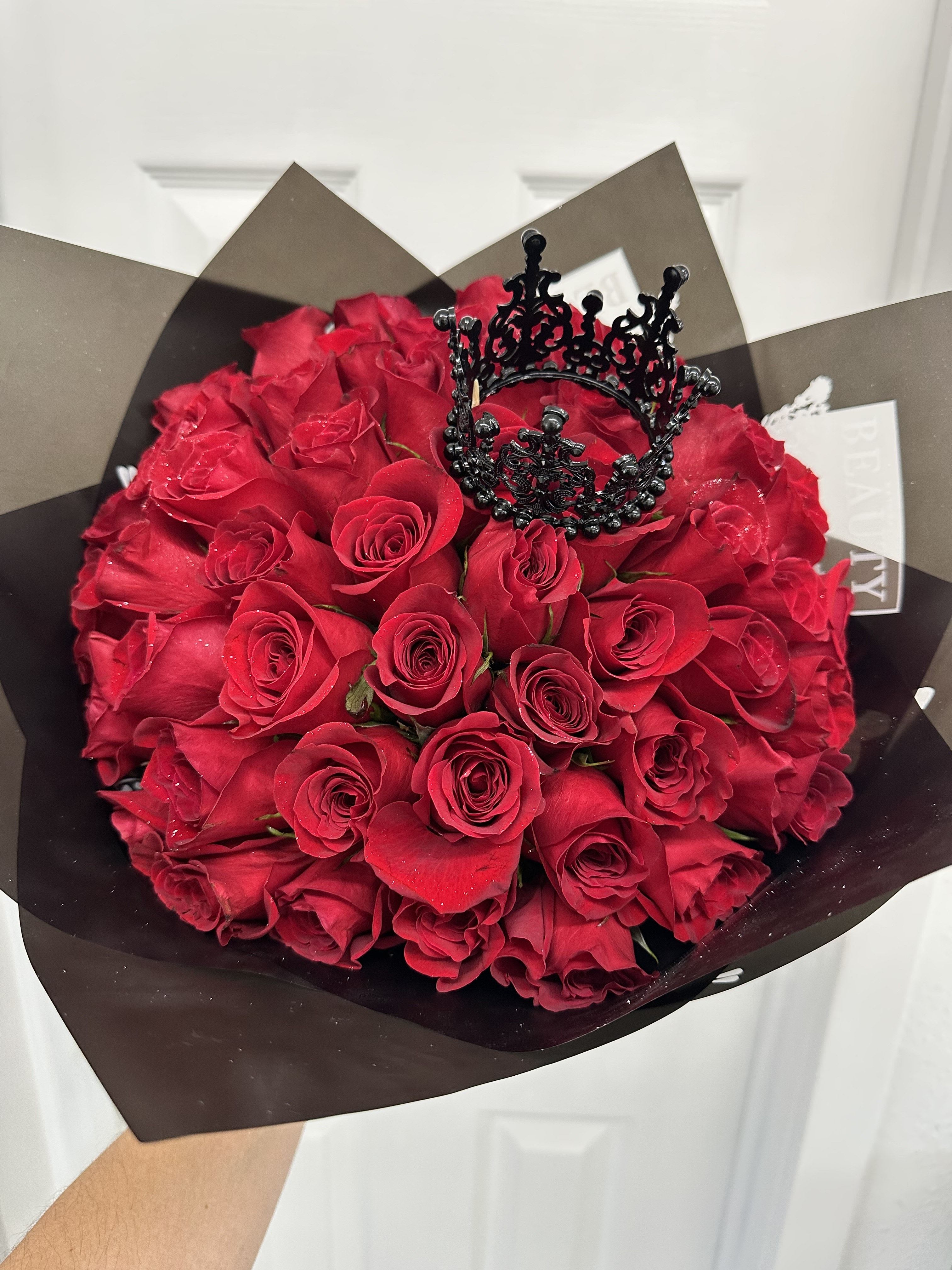 Bouquet of red roses wrapped in dark paper with a black crown topper