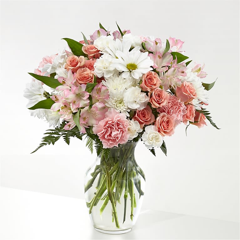 Sweet Peach Serenade - A soft, romantic bouquet in gentle pinks and whites-Sweet Peach Serenade is a birthday bouquet, anniversary arrangement, or Mother's Day gift that will make the person you're thinking of feel cherished. The rounded, full shape puts large white daisy-like blooms front and center, with clusters of pink roses, carnations, and pale alstroemeria layered for a tender, celebratory mood that also works beautifully as a get-well or springtime surprise.  Arranged in a clear glass vase, the design feels airy and classic: the transparent vase shows stems and water for a fresh, garden-picked look. Expect a lush mix of textures-velvety rose petals, ruffled carnations, delicate alstroemeria, and the brighter daisy forms-woven with soft green foliage to lift the pastel palette. This is the kind of bouquet that reads as thoughtful and intimate; choose it when you want her to feel truly seen and gently celebrated.
