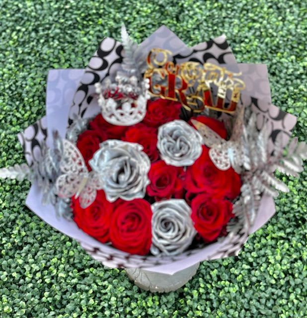 Congrats Grad Platinum Rose Bouquet  - A bold, celebratory rose bouquet that announces achievement with flair: tightly packed red roses paired with metallic silver roses form a striking red-and-silver arrangement perfect as a graduation bouquet, anniversary gift, or Valentine's surprise. The compact, rounded shape and dramatic palette give the recipient an immediate sense of occasion-the kind of bouquet that makes them feel honored and celebrated.  This arrangement mixes classic red roses with several metallic silver roses for high-contrast visual impact, finished with decorative butterfly picks and printed wrapping paper for a stylized, embellished look. The presentation is lush and full, delivered in a compact, rounded shape that reads as both elegant and festive. Ideal for grads, loved ones marking a milestone, or anyone you want to acknowledge with something showy and joyful-no special care beyond fresh water is needed to keep the roses looking their best in the days after delivery.