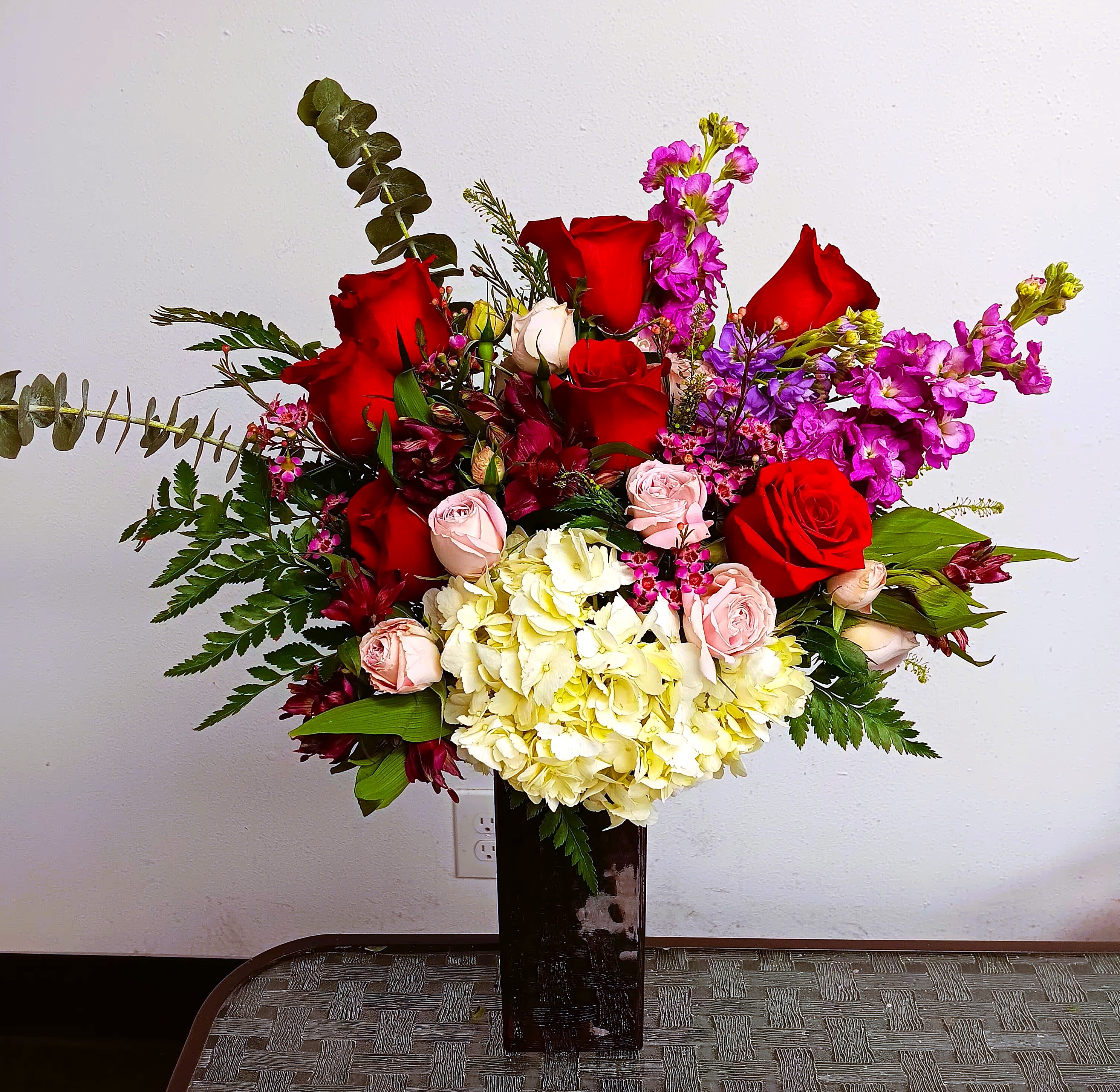 Large bouquet of red and pink roses with pale hydrangeas in a tall vase
