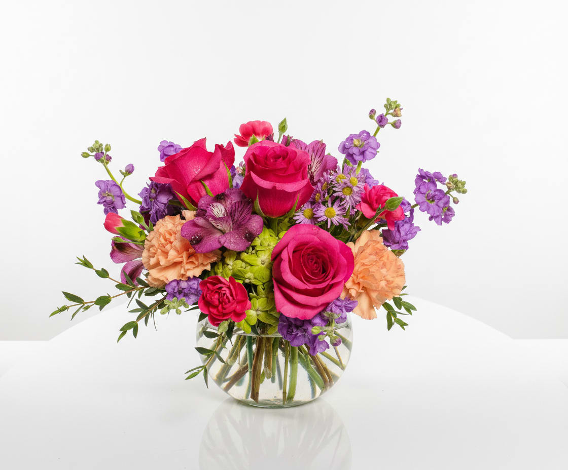Mixed bouquet of pink and purple flowers in a round glass vase