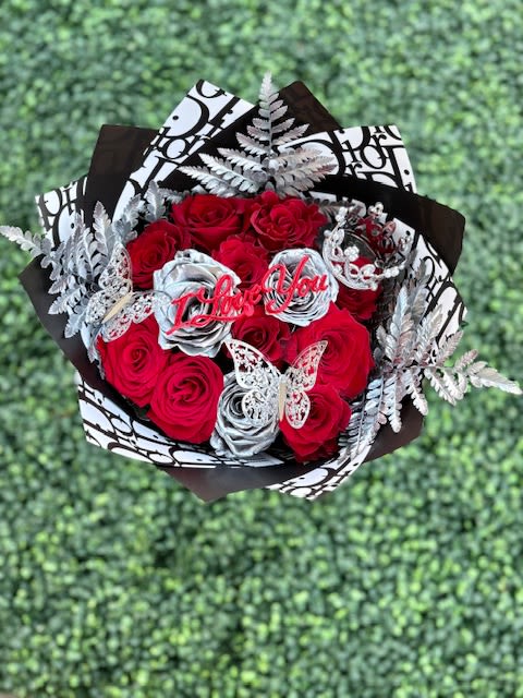 I love you Platinum Bouquet Ramo - Tightly clustered red roses-punctuated by a few metallic silver roses-create a dramatic, romantic statement that's perfect for an anniversary or Valentine's Day bouquet. This "I love you" platinum-style arrangement reads as both passionate and elegant, the kind of gift that makes the person you're thinking of feel adored and celebrated the moment they see it.  Wrapped in bold black-and-white patterned paper and trimmed with silver fern-like sprays, the bouquet is finished with butterfly picks and a pink "Thank You" topper for a playful, gift-ready touch. The mix of deep red, bright white highlights, and metallic accents gives striking contrast and texture; roses are arranged tightly to maximize visual impact and presence. Ideal for anniversaries, romantic surprises, or a heartfelt thank-you, this arrangement arrives ready to present-no extra wrapping needed-and will keep its classic rose look for several days with fresh water and a cool spot away from direct sunlight.