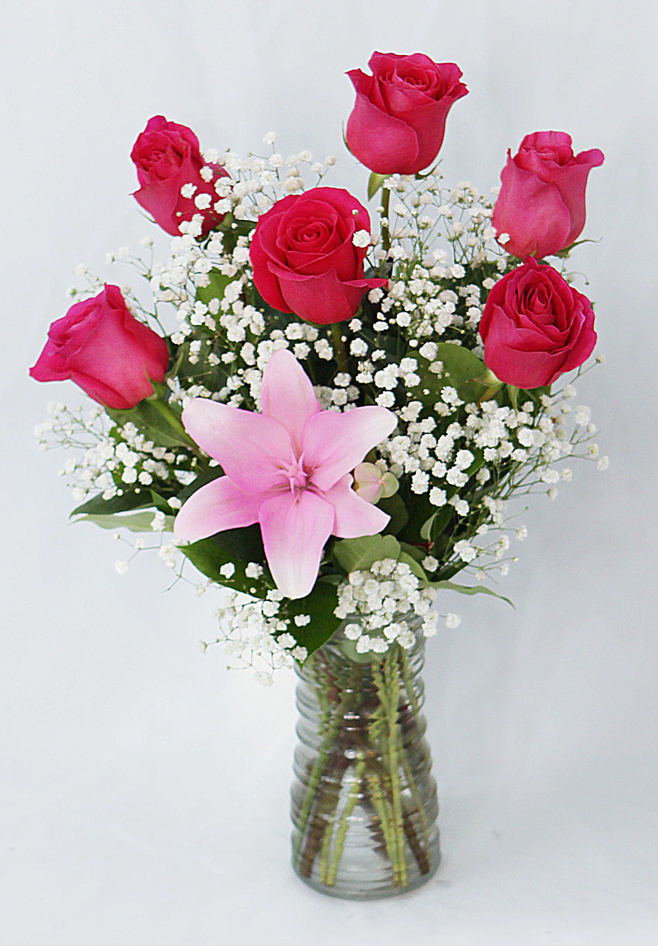 Pink roses and a lily in a glass vase with white baby's breath