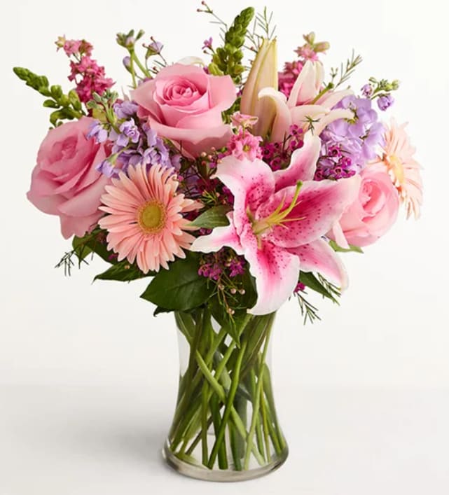 Always On My Mind - Soft pink roses and pink-and-white lilies mingle with pale peach gerbera and clusters of delicate purple stock in a full, rounded flower arrangement-perfect as a birthday bouquet, Mother's Day gift, or a thoughtful "thinking of you" surprise. The colors read soft and romantic, so the person you're sending it to will feel gently celebrated and remembered the moment they see it.  Layered at varying heights for a lush, garden-style look, this everyday arrangement is presented in a clear glass vase that keeps the presentation clean and classic. The mix of roses, lilies, gerbera daisies, and purple filler creates a textured, fragrant display in pinks, lavenders, white accents, and fresh green foliage-an easy, elegant choice for thank-you, anniversary, or spring celebrations.