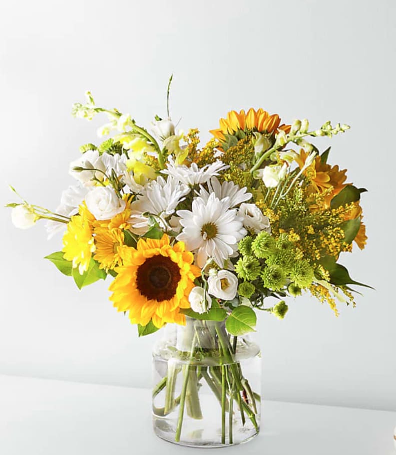 Bouquet of sunflowers, white daisies, and yellow flowers in a clear glass vase