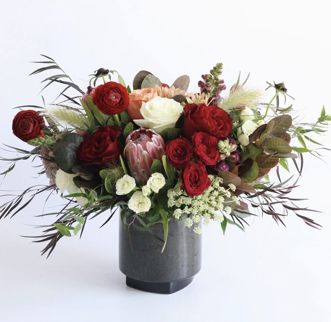 Arrangement of red and cream roses with protea and other blooms in a dark gray vase