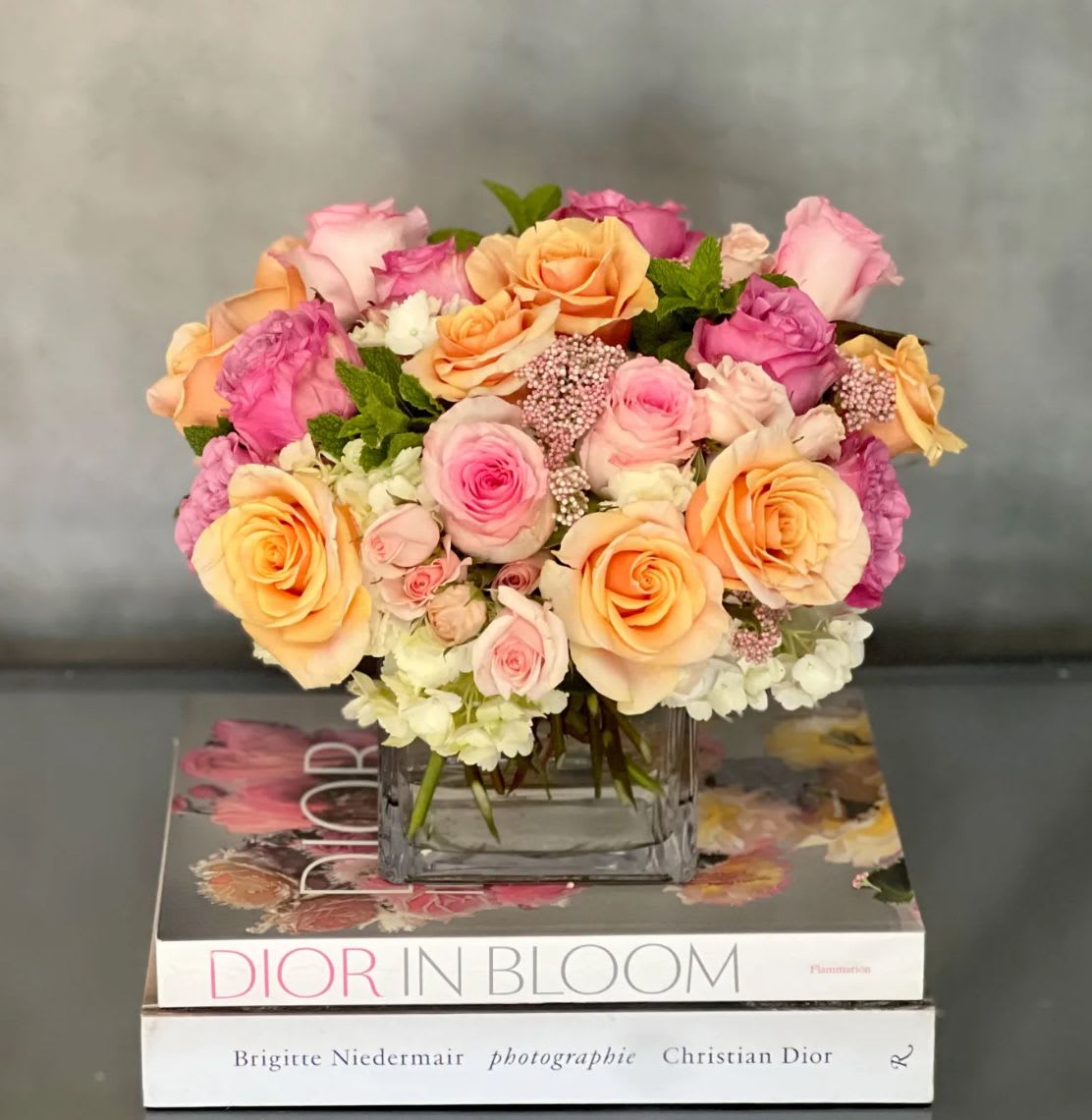 Low arrangement of peach and pink roses in a glass vase set on fashion books