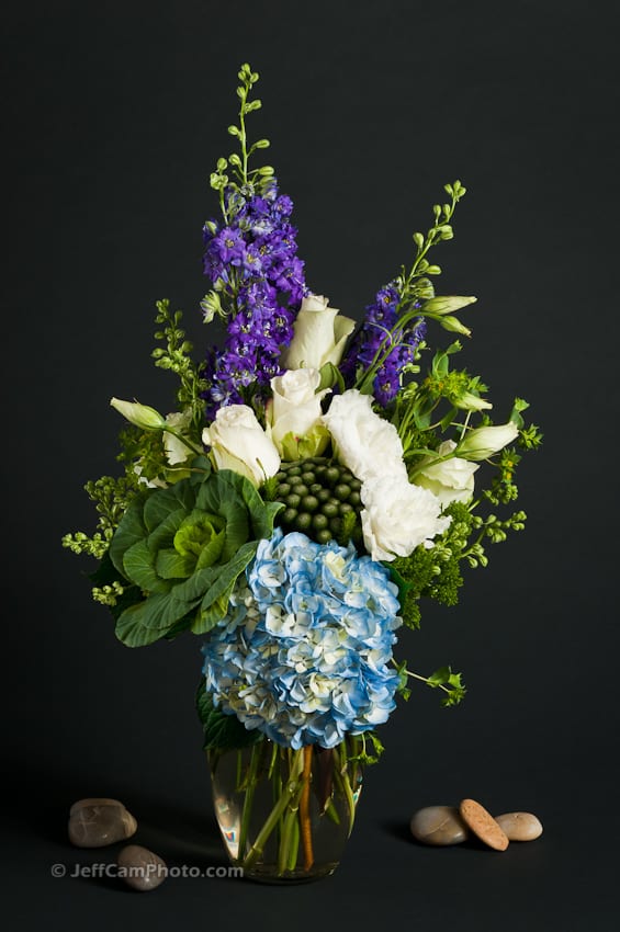 Tall bouquet of blue hydrangea, white roses, and purple flowers in a glass vase