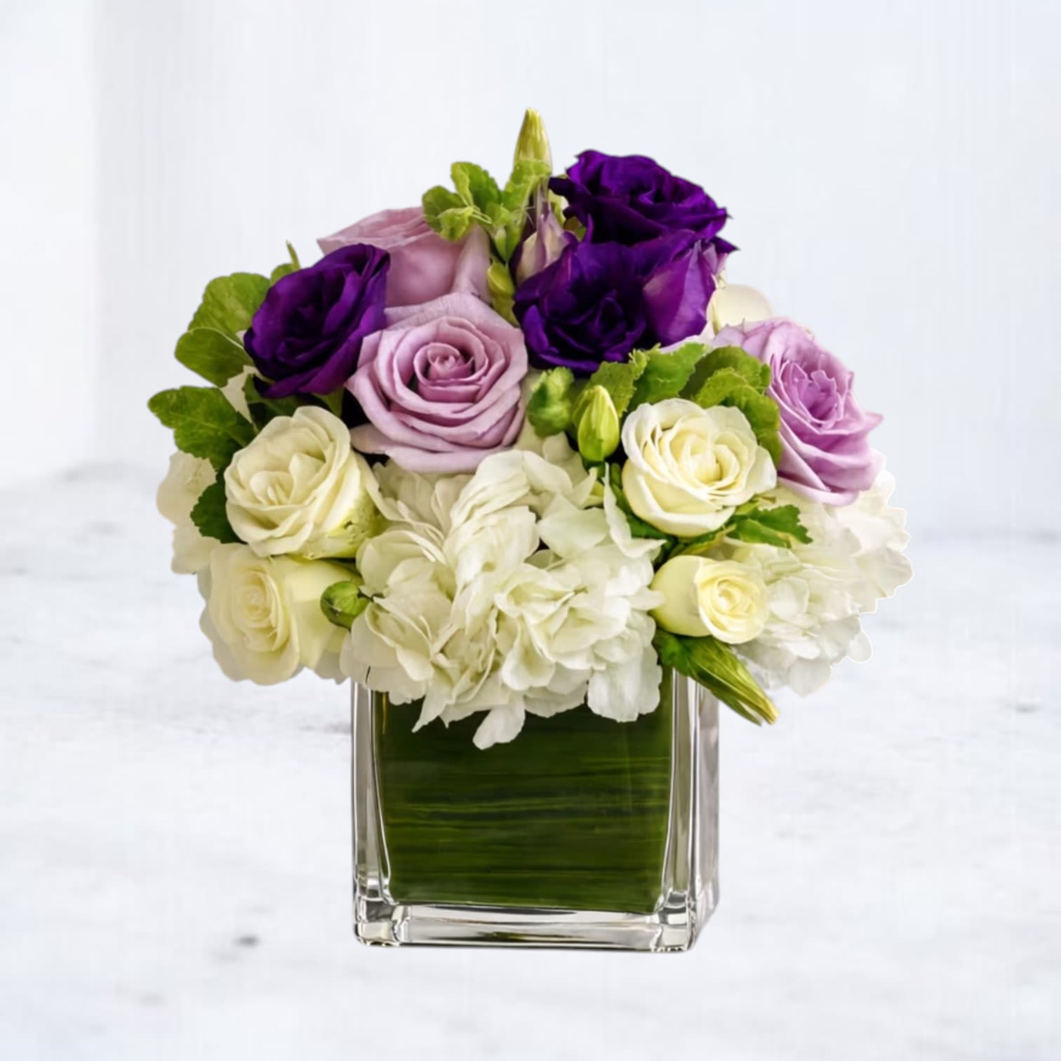 Purple, lavender, and white roses in a square glass vase