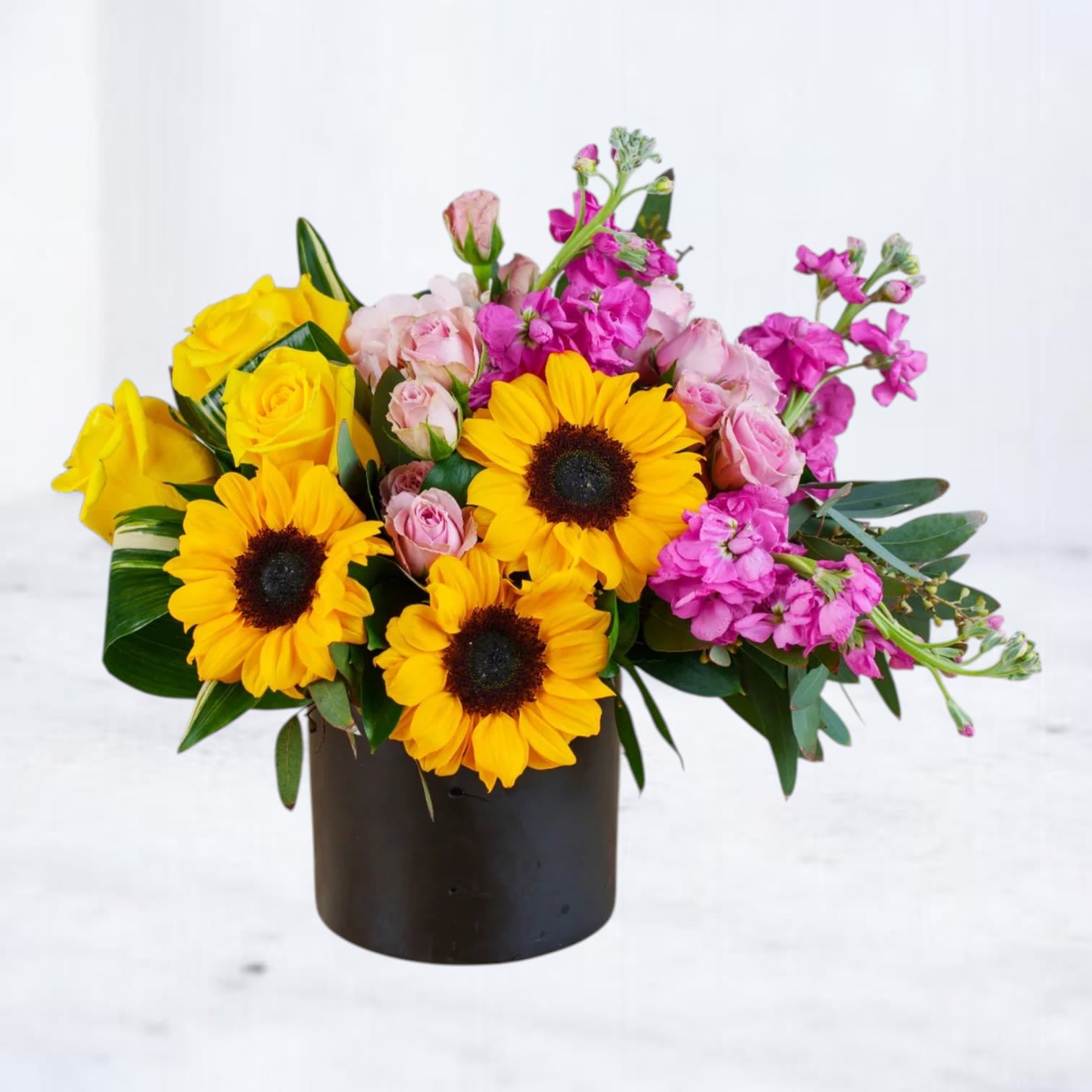 Pink Cadillac - Pink Cadillac is a bold, feel-good floral arrangement featuring cheerful sunflowers, vibrant yellow roses, blush spray roses, hot pink stock, and fresh seasonal greenery designed in a sleek modern black vessel. Bursting with sunny yellows and electric pinks, this arrangement brings a playful retro-inspired energy with a fresh editorial edge.  Perfect for birthdays, celebrations, thank-you gifts, get-well flowers, or brightening someone’s day, Pink Cadillac combines classic happy blooms with modern floral styling for a design that feels vibrant, stylish, and unforgettable. Crafted with premium seasonal flowers and lush textures for fullness and movement.  Available for same-day flower delivery in Magnolia, The Woodlands, Montgomery, Conroe, Spring, Tomball, and surrounding Houston areas.