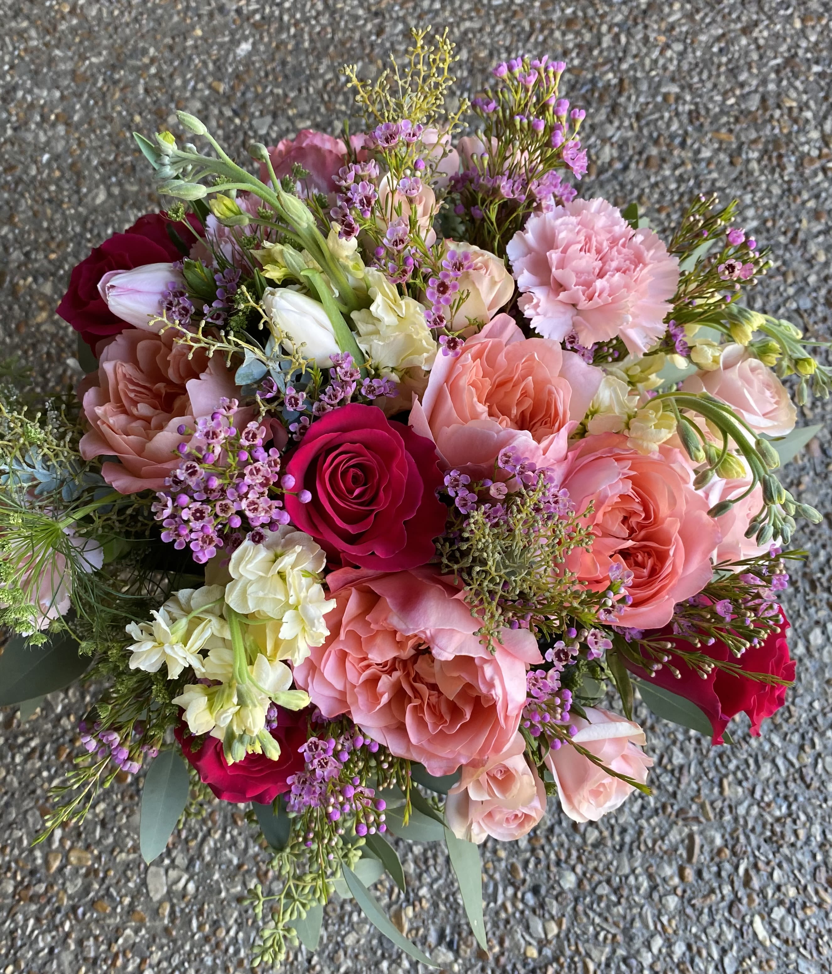 Sophia's Pink Lace Bouquet - A lush, rounded flower arrangement that reads as both romantic and cheerfully everyday, this pink-and-red bouquet is perfect as an anniversary roses gift, a birthday bouquet, or a just-because surprise. Sophia's Pink Lace Bouquet centers on garden roses and classic roses in blush, coral and vivid red tones that create a striking contrast, making the recipient feel truly seen-whether you're saying "I love you," "thank you," or "thinking of you" after a long week.  The design mixes garden roses, spray roses, tulips, carnations and small pale filler blooms with soft purple accents and airy sprigs for texture. Broad eucalyptus-like greenery spills outward from a clear glass vase for a full, hand-tied silhouette that looks abundant on a dining table or bedside. The palette of pinks, creams, reds, whites and greens brings both warmth and cheer-suitable for Spring and Summer moments as well as Memorial Day remembrances.  Ideal for sending congratulations at graduation, a sweet new-baby welcome, a thoughtful get-well gesture, or a sympathy bouquet that still feels gentle and uplifting, this arrangement arrives ready to display. Vase included; to extend bloom life, trim stems and refresh the water every couple of days-this is the kind of bouquet that brightens a room and makes the person you care about feel celebrated.