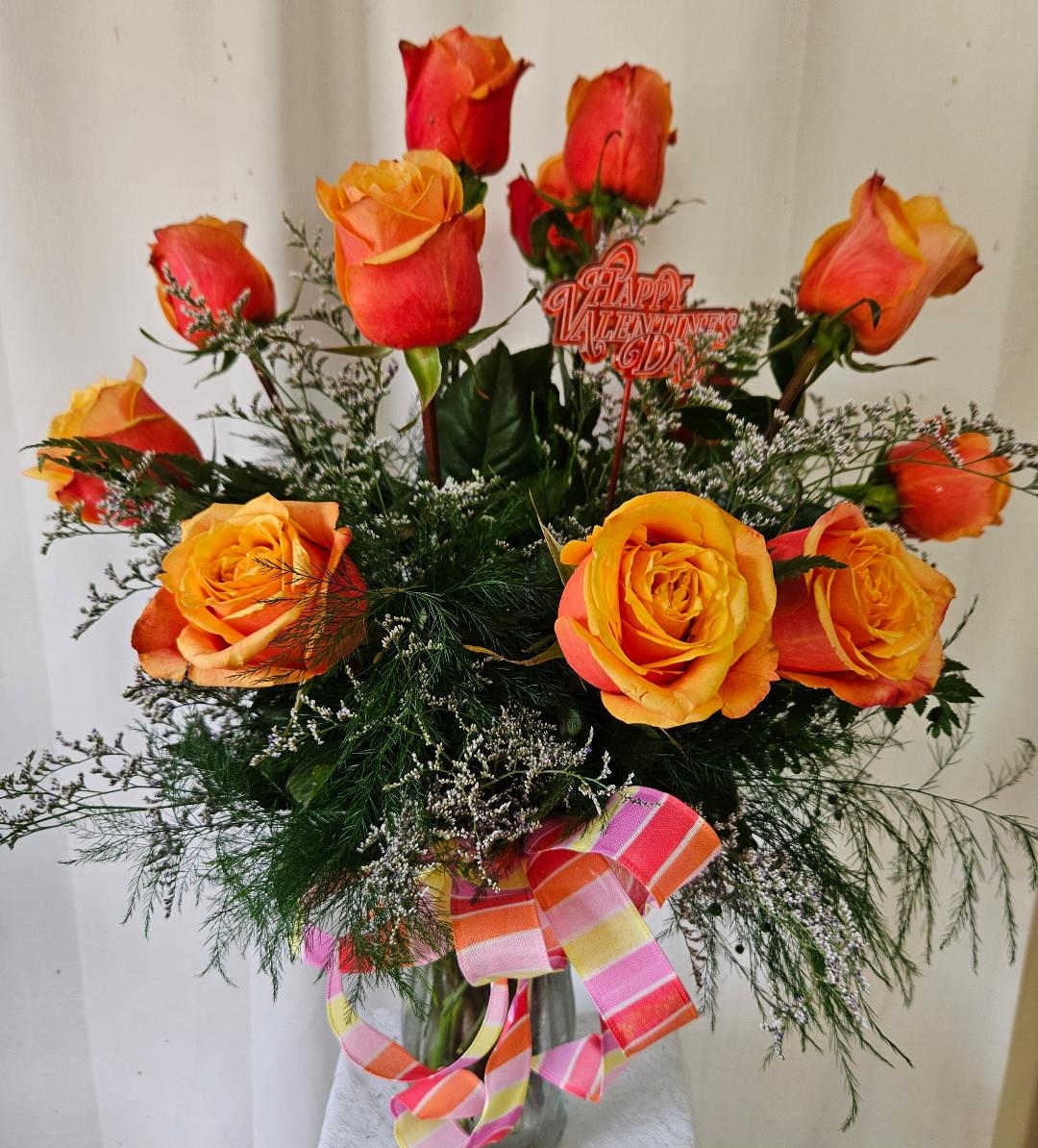 Cherry Brandy Sunset Elegance Bouquet - Indulge in the rich hues of a breathtaking sunset with our Cherry Brandy Sunset Elegance Bouquet, a stunning arrangement designed to captivate the senses and ignite the imagination. Nestled within a sleek vase wrapped in a matching bow, this exquisite ensemble is a symphony of color and texture, sure to leave a lasting impression.  At the heart of this captivating bouquet are a dozen Cherry Brandy roses, their velvety petals boasting a mesmerizing blend of crimson and amber. Enhanced with accents of delicate tree fern and ethereal misty, each bloom exudes an air of sophistication and allure, reminiscent of a romantic evening sky.  Wrapped in a coordinating bow, the vase serves as a striking backdrop for this radiant arrangement, adding an extra touch of elegance and refinement to the display.  Whether presented as a gesture of love or appreciation, our Cherry Brandy Sunset Elegance Bouquet is the perfect choice for any occasion. Let its beauty and grace illuminate your loved one's day and convey your heartfelt sentiments with style and sophistication.