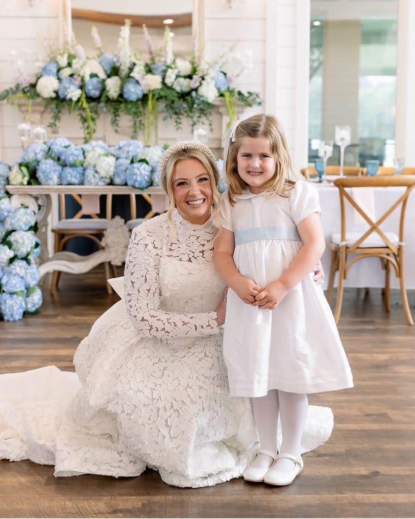 Bride and young girl in white dresses posing before blue and white floral decor