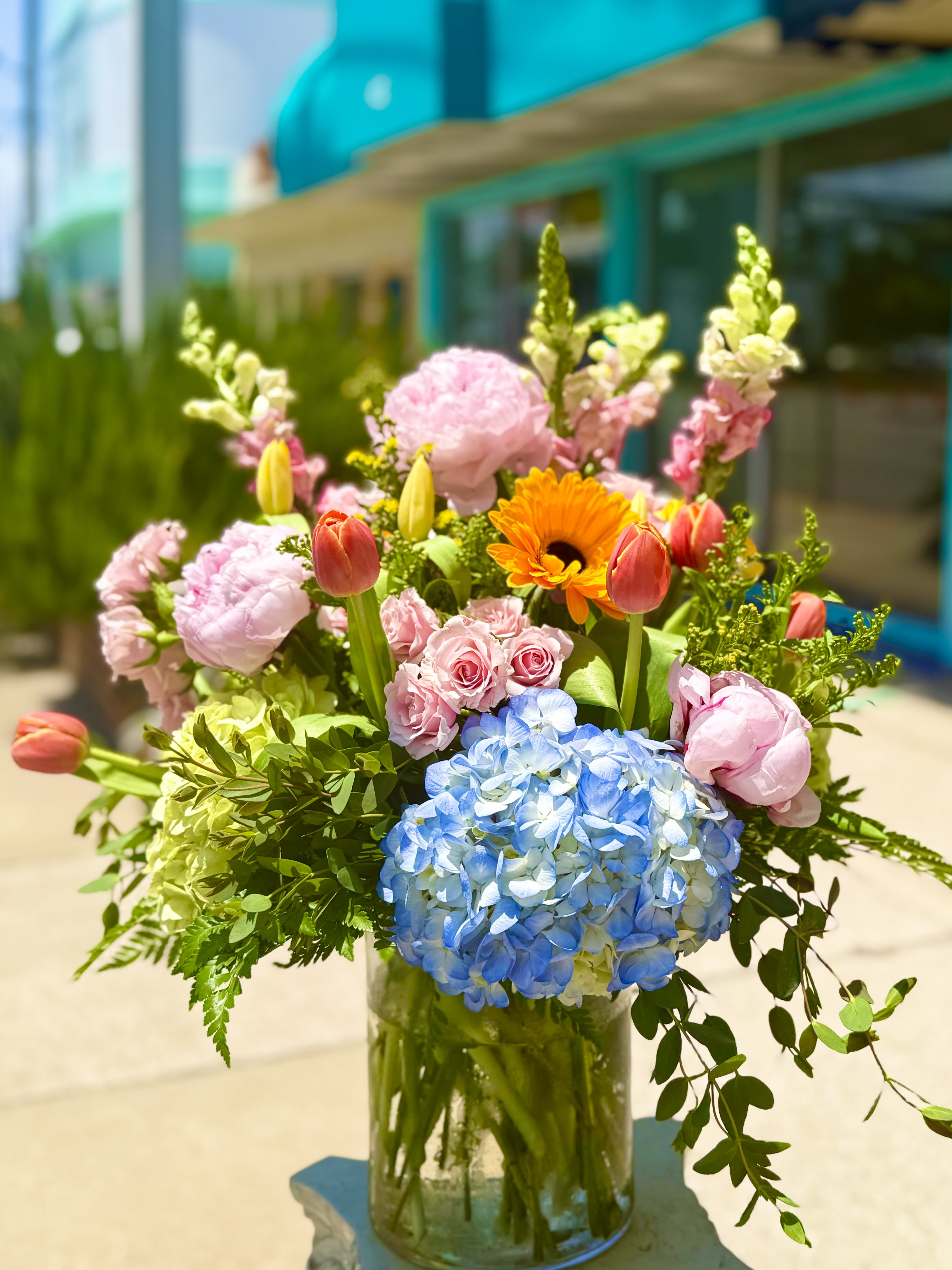 Mixed bouquet in a glass vase with blue hydrangea, pink roses, tulips, and orange gerbera daisies