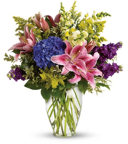 Bouquet of pink lilies, blue hydrangea, and purple flowers in a clear vase