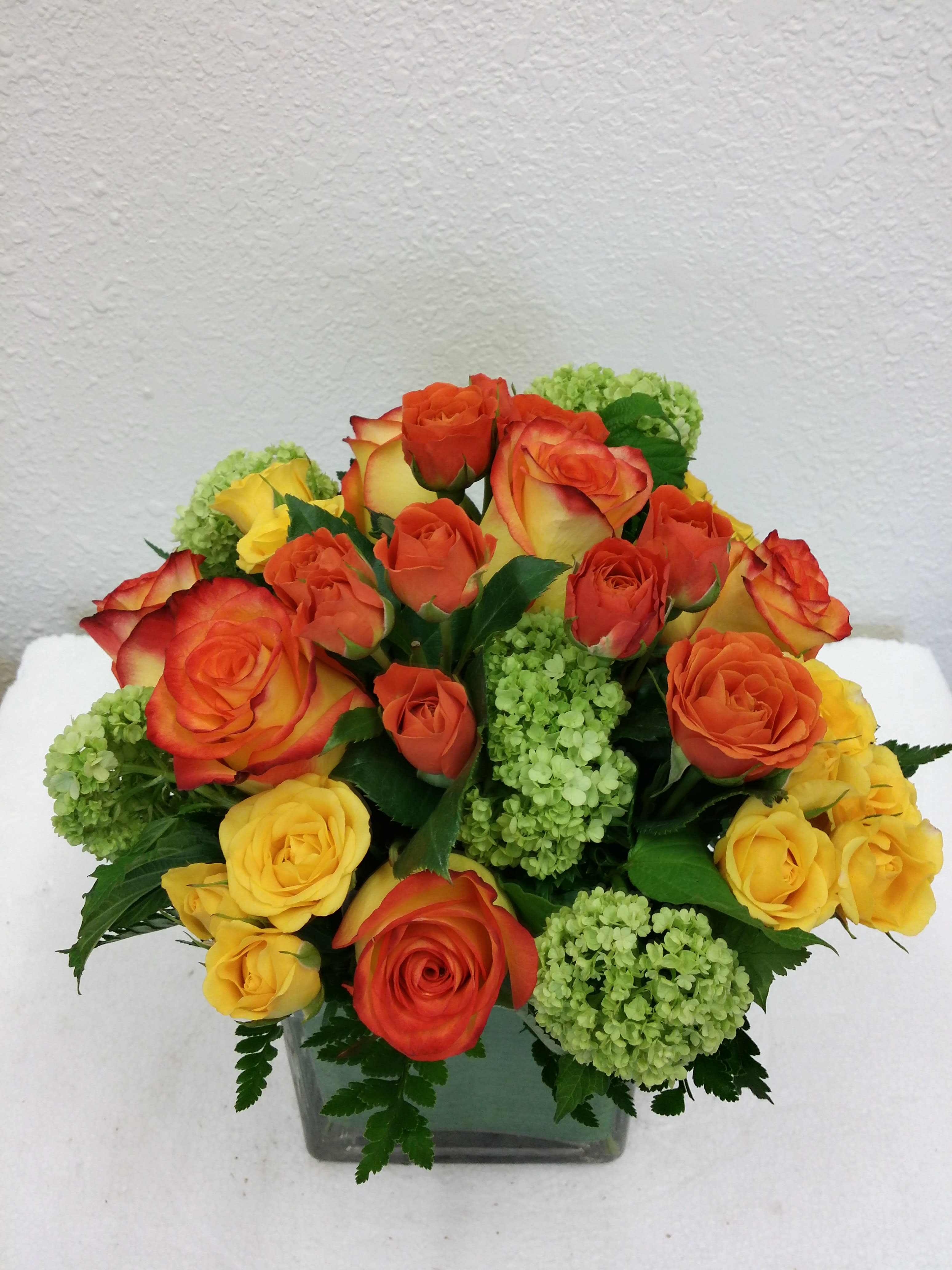Bouquet of orange and yellow roses with green hydrangeas in a square glass vase