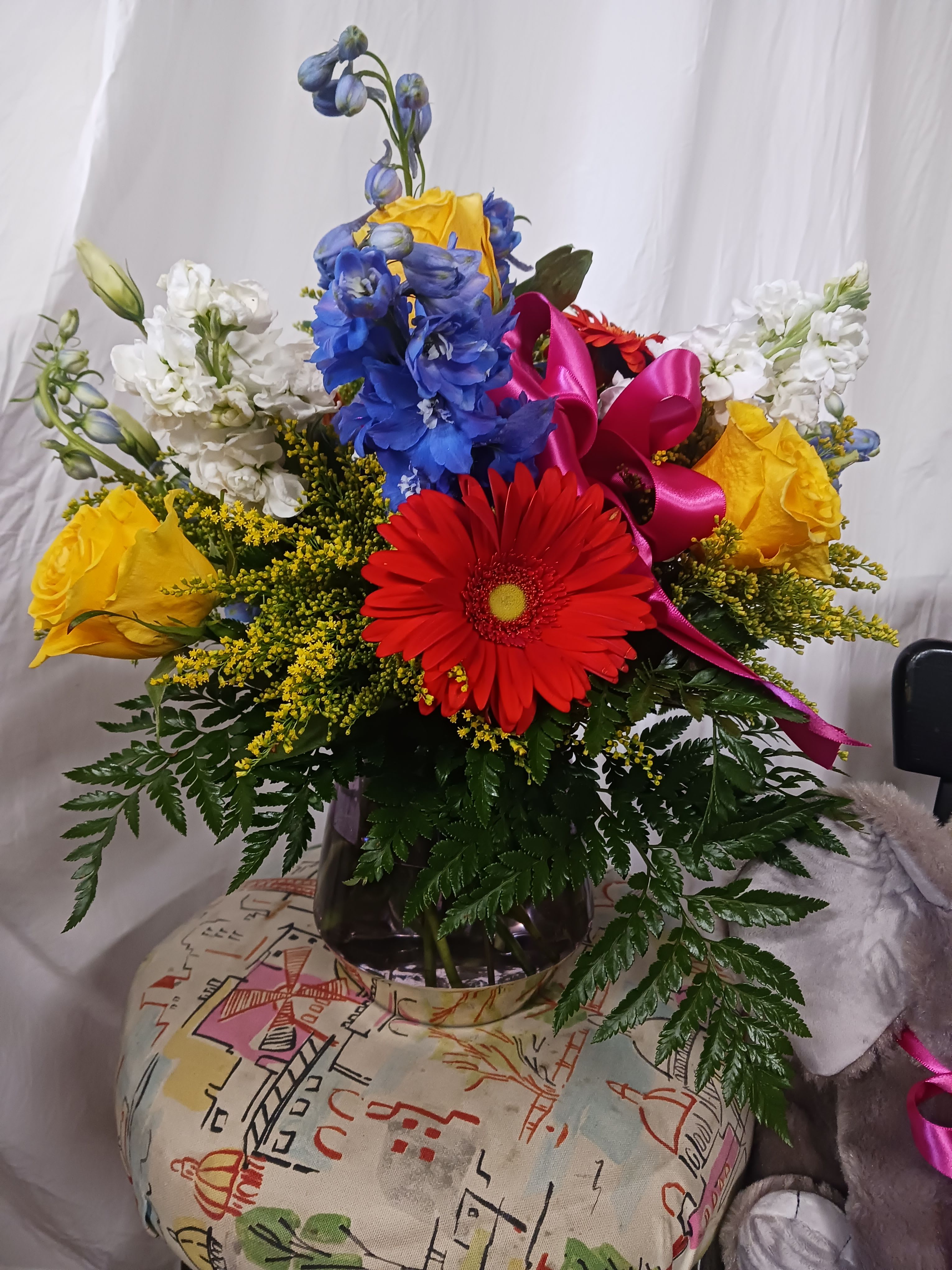 Brighter - Bright mix of flowers in a vase.  Gerbera daisies, blue Delphinium, white stock and yellow roses with filler flowers and greenery.