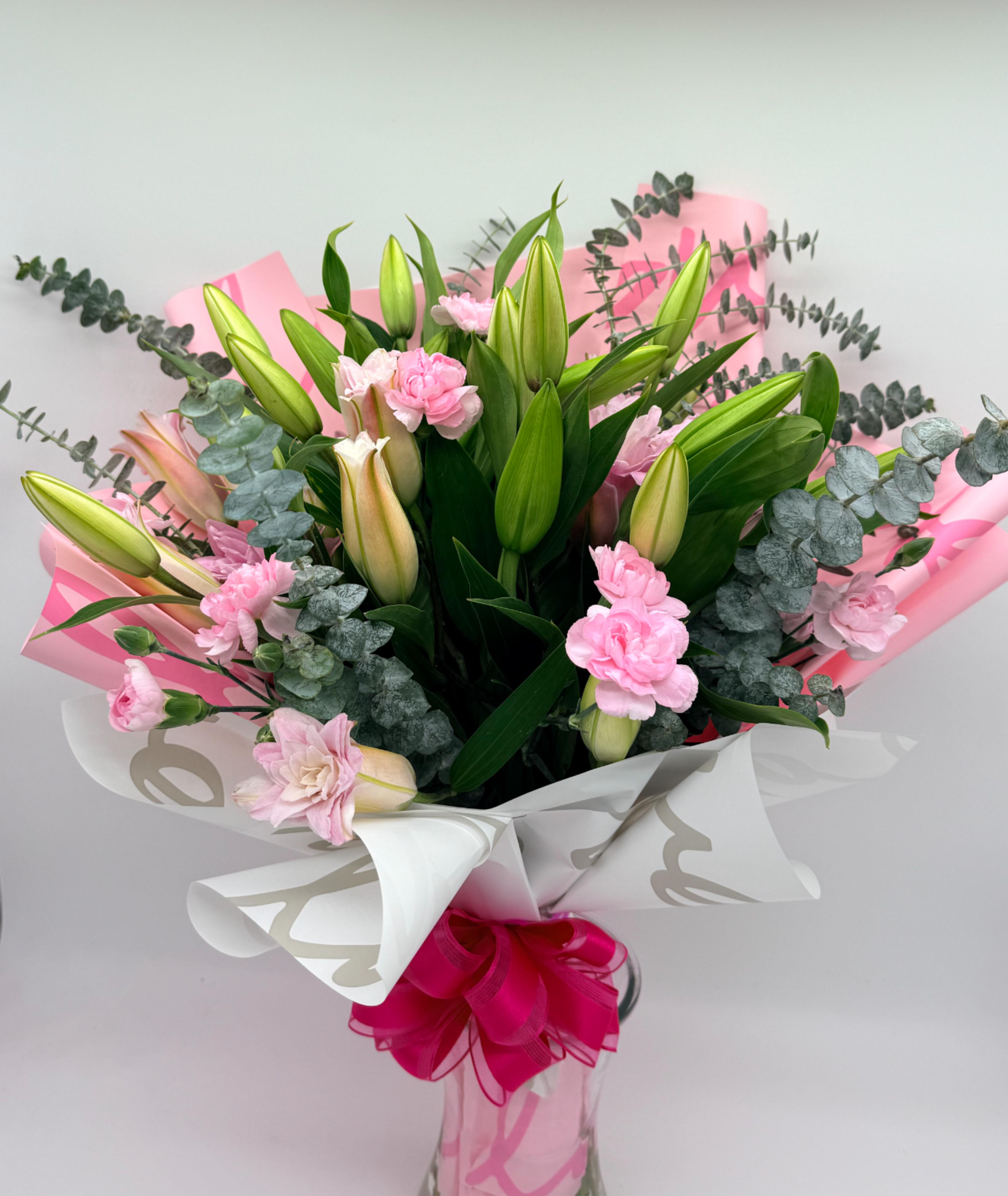 Sweet Lily Garden - A lush wrapped bouquet of pink lilies, carnations, and greenery, tied with a bow for a joyful finish.  Perfect for celebrating life’s sweetest moments.  No vase Included but available for add on. Flower selection may vary depending on availability.