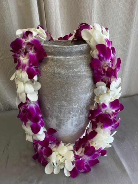 Purple and white orchid lei draped over a gray vase