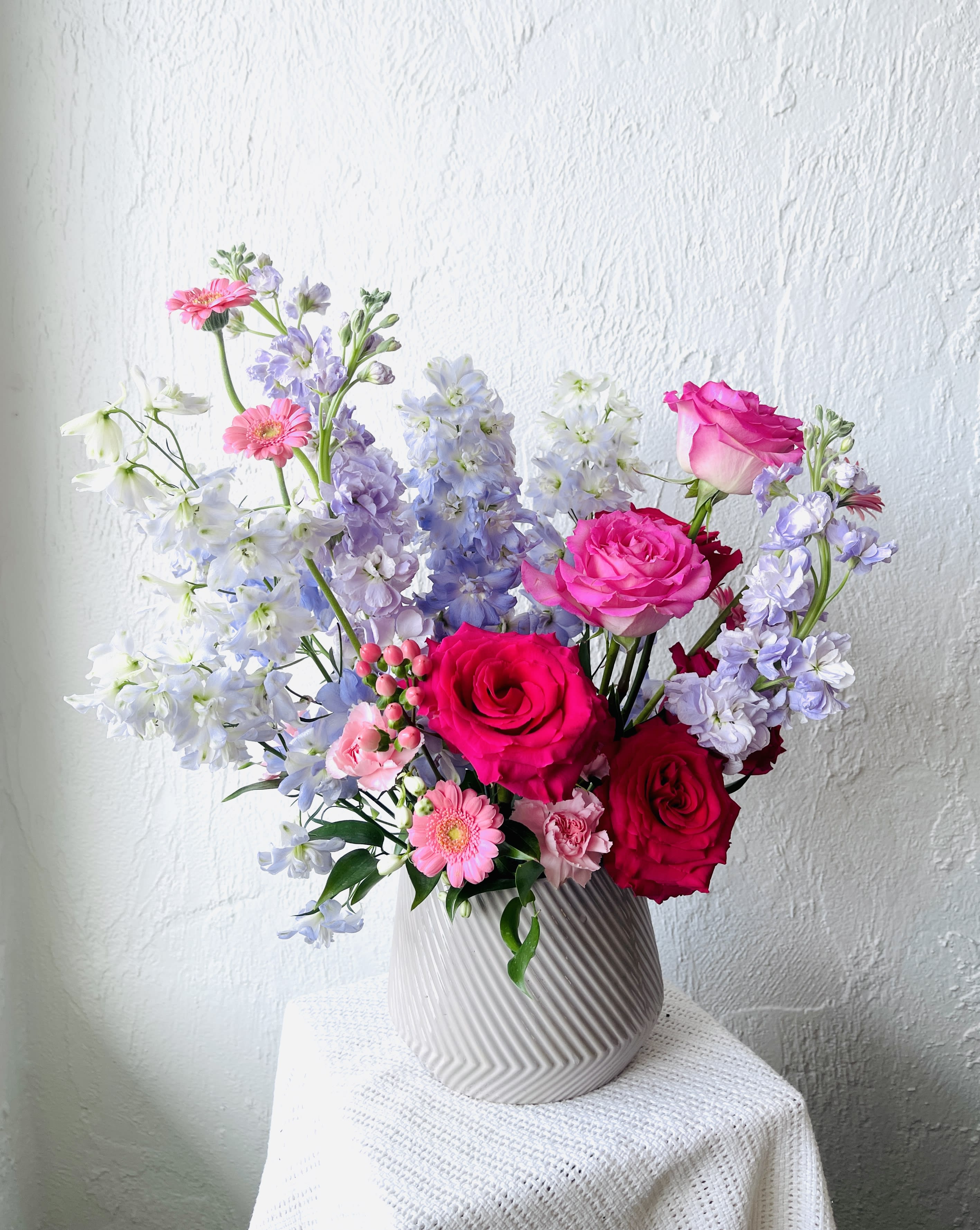Bouquet of pink roses, lavender blooms, and white flowers in a ribbed vase