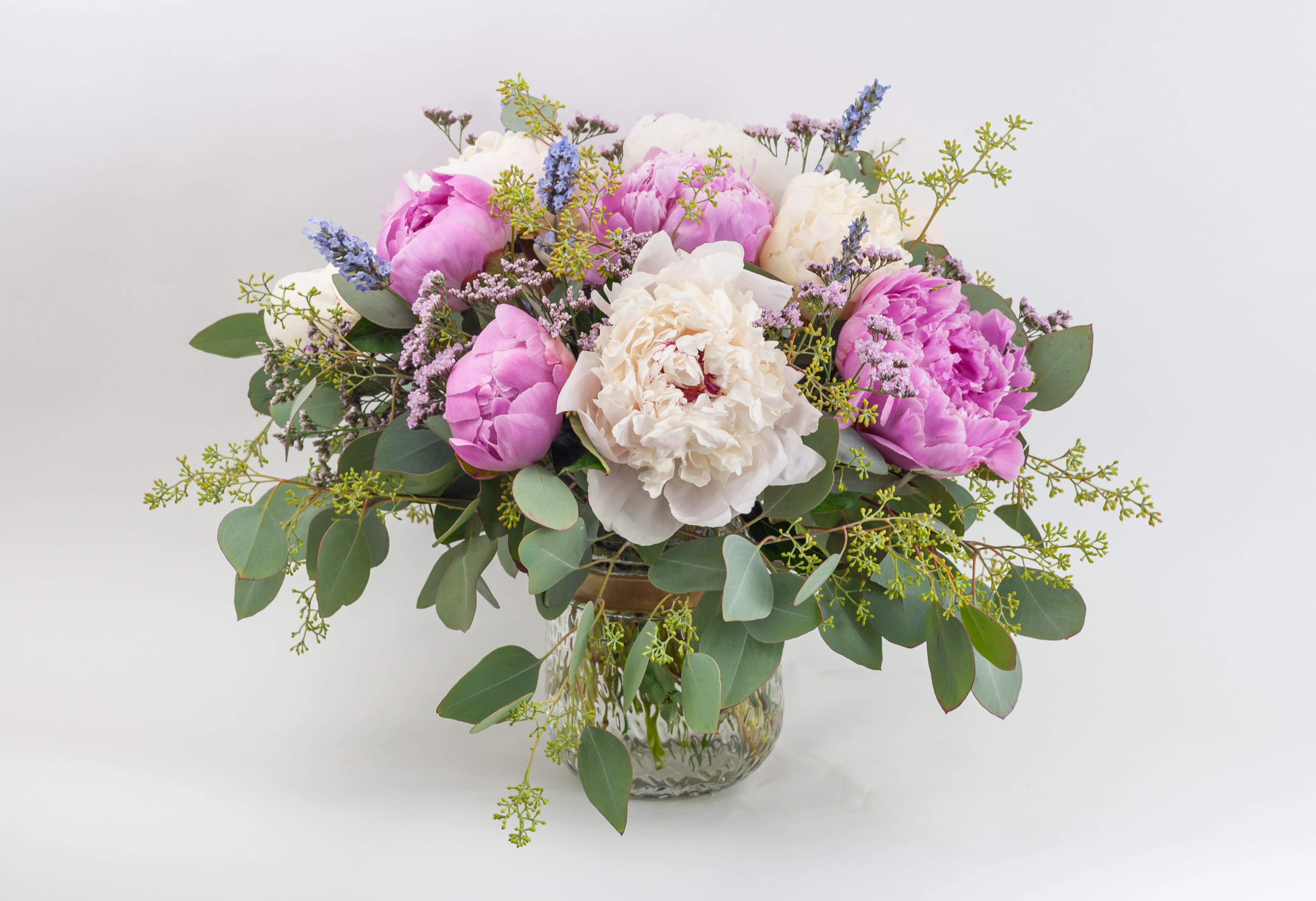 Low glass vase arrangement with pink and white blossoms and purple accents in a loose, full design