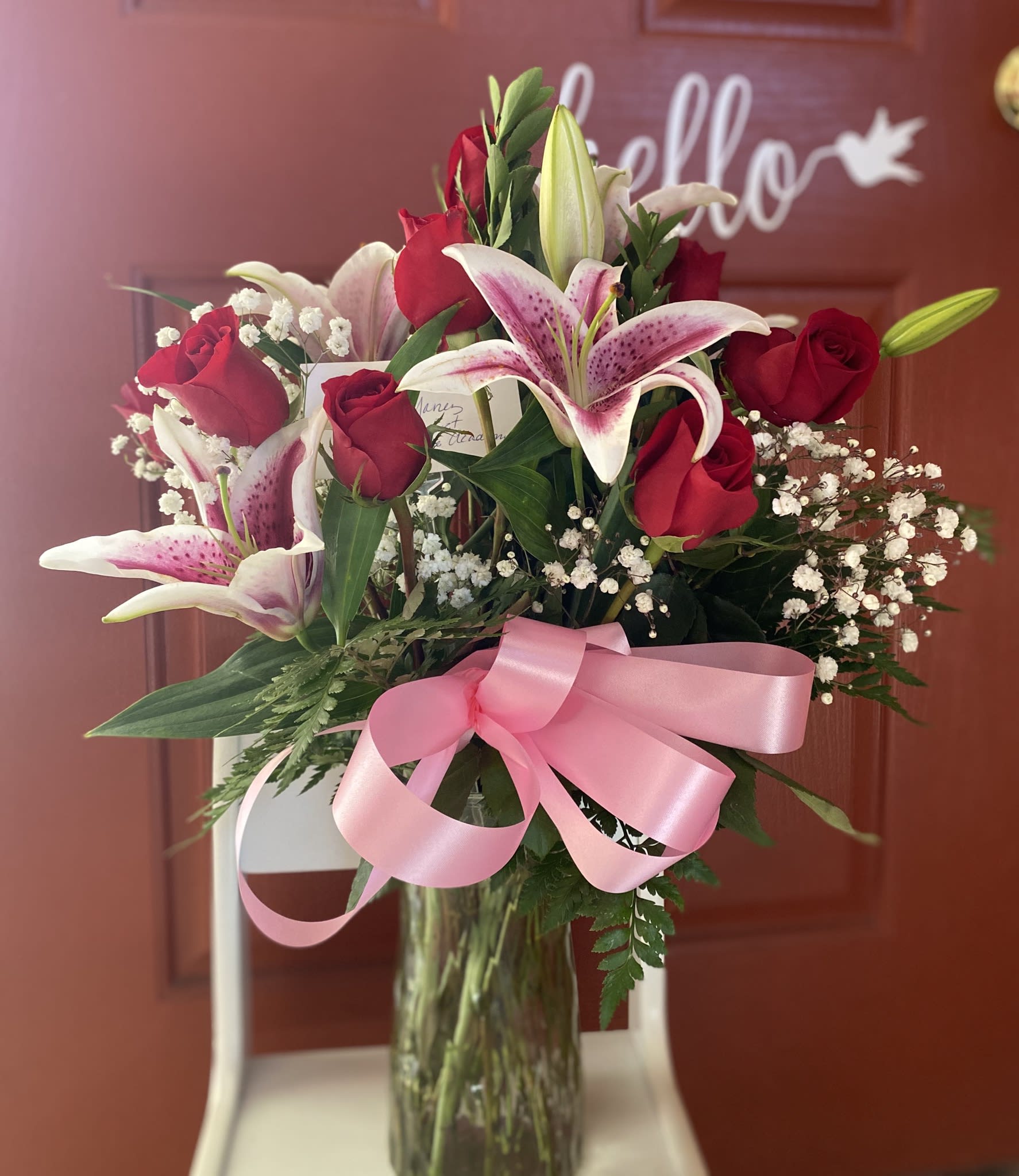 Bouquet of red roses and pink lilies in a glass vase with a pink ribbon