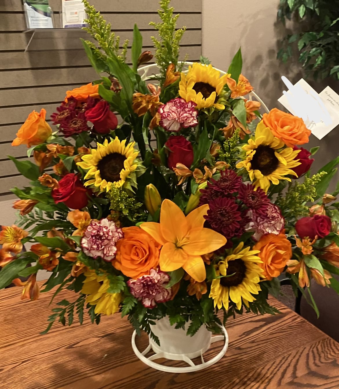 Mixed bouquet in a white container with sunflowers, roses, and lilies