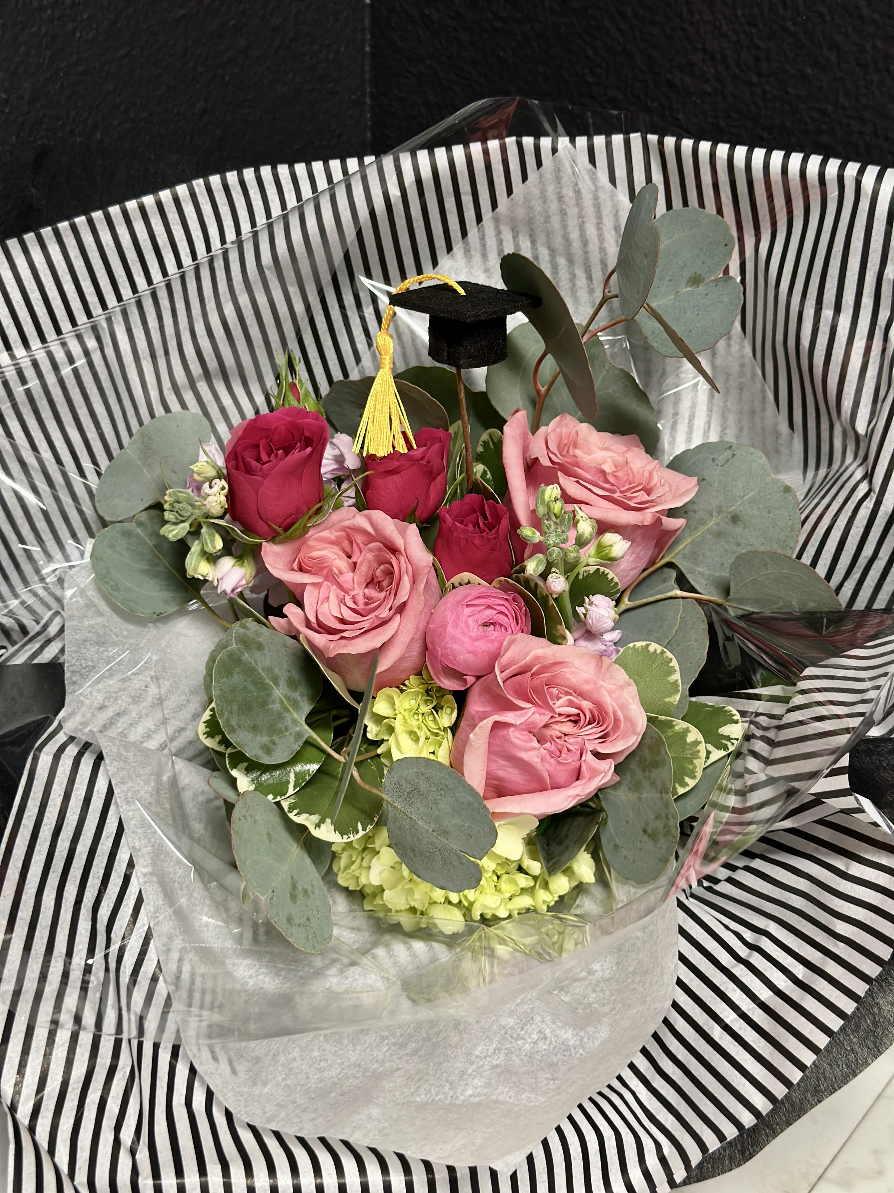Graduation Paper Wrap Bouquet- Pink  - Celebrate your Grad with a pretty paper wrapped bouquet in shades of Pink. Stems and a super cute mini graduation cap pick are wrapped in our fancy tissue papers &amp; placed on a temporary water source. Give us a call if you're hoping for another color option. 