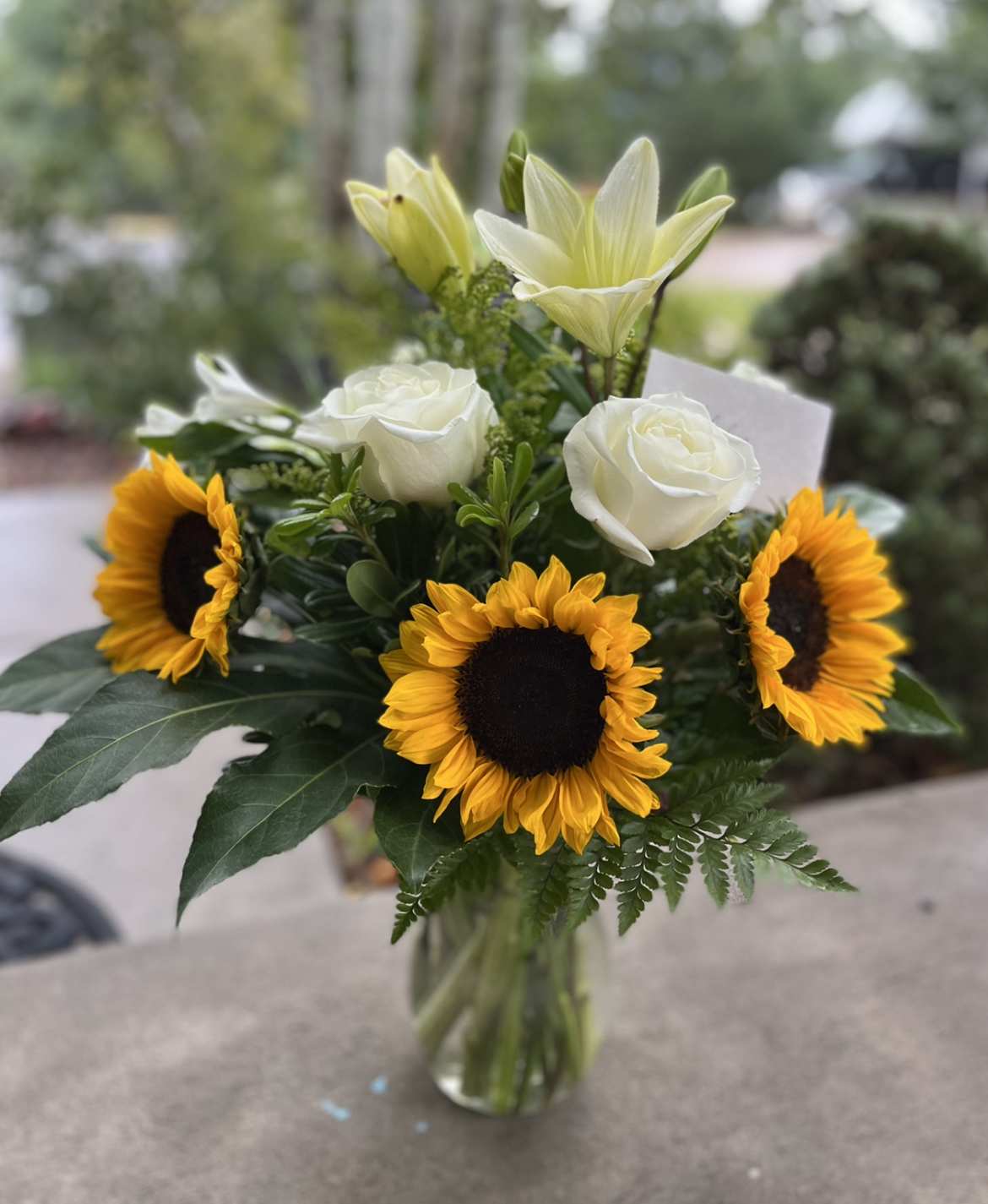 Bouquet of sunflowers, white roses, and pale lilies in a glass vase
