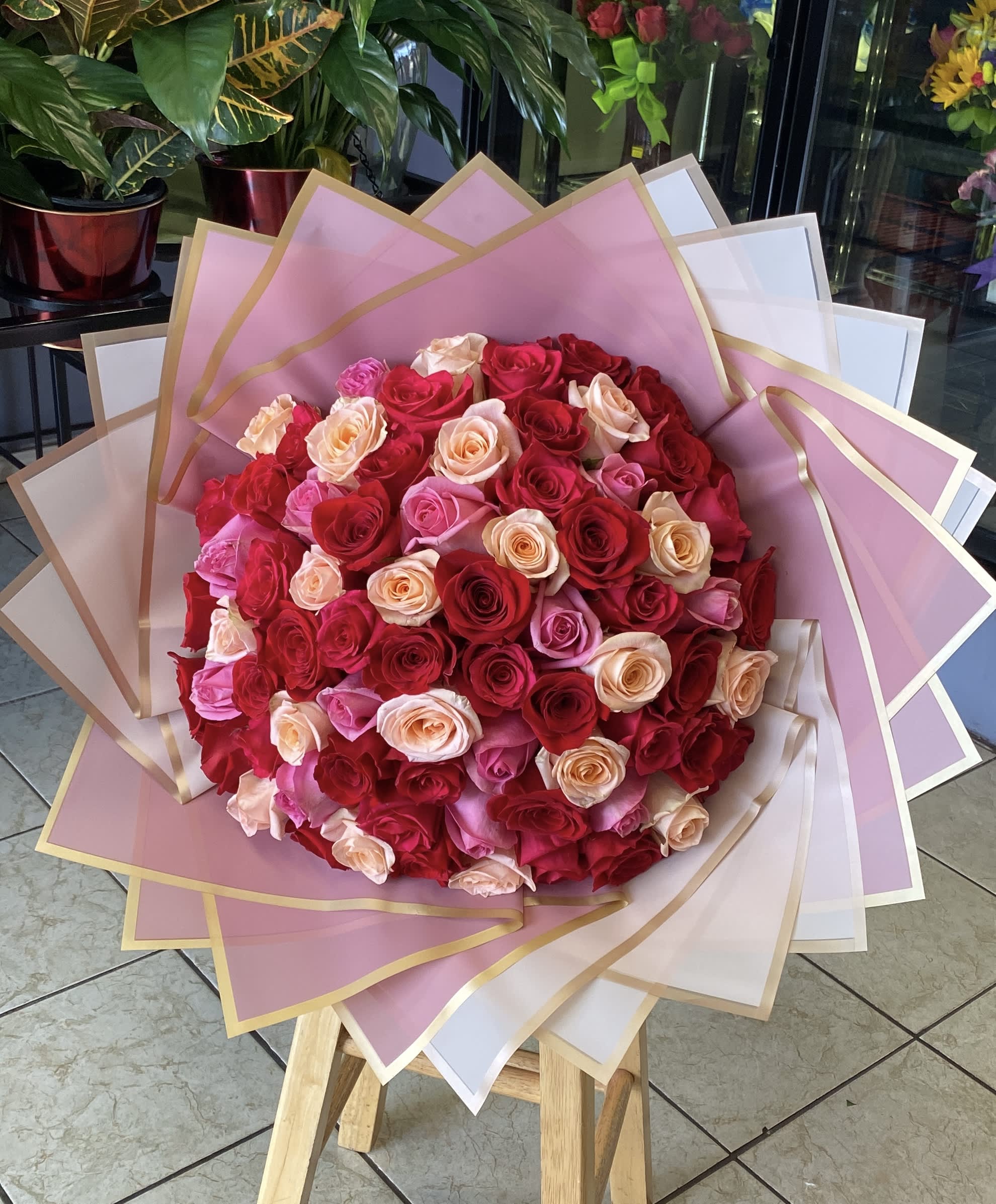 Large bouquet of red, pink, and peach roses wrapped in pink paper