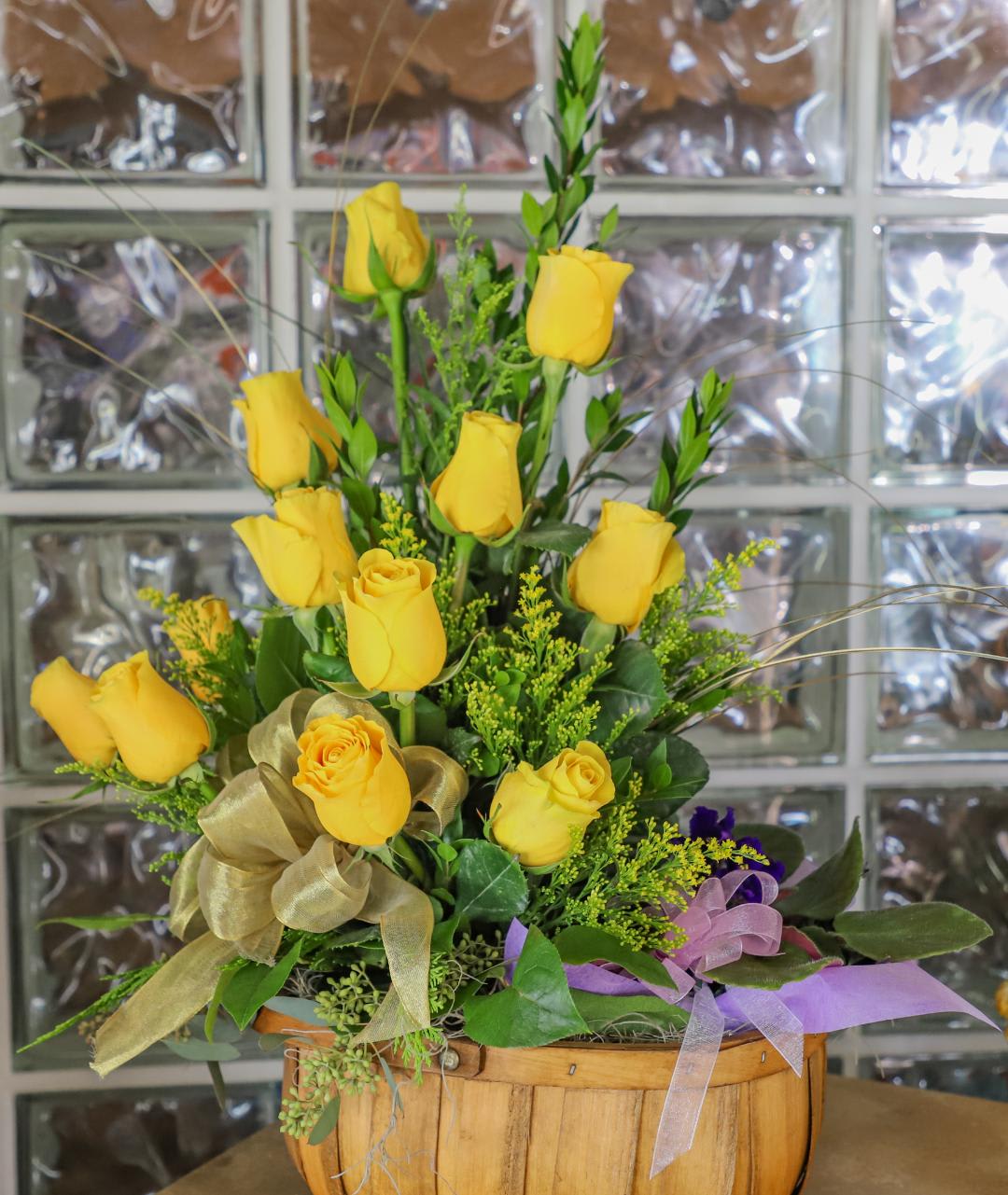 Yellow roses arranged in a wooden basket with ribbon accents