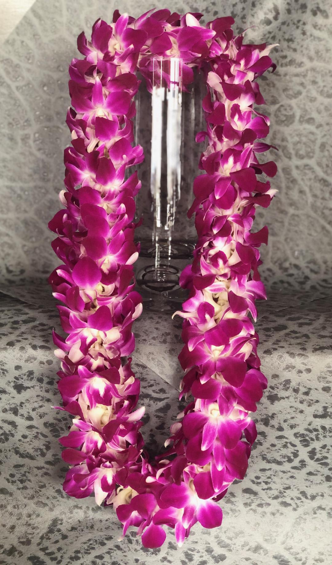 Purple orchid lei draped around a clear glass vase