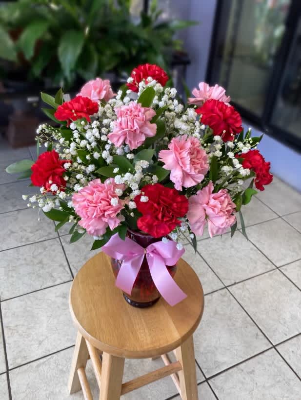 Pink and red carnations in a glass vase with a pink ribbon